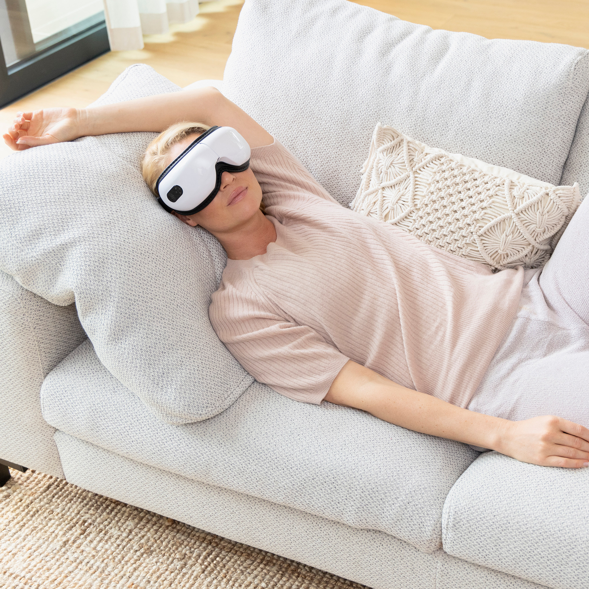 Una mujer con una máscara para dormir yace en un sofá. Su brazo está extendido. Una almohada descansa junto a ella.