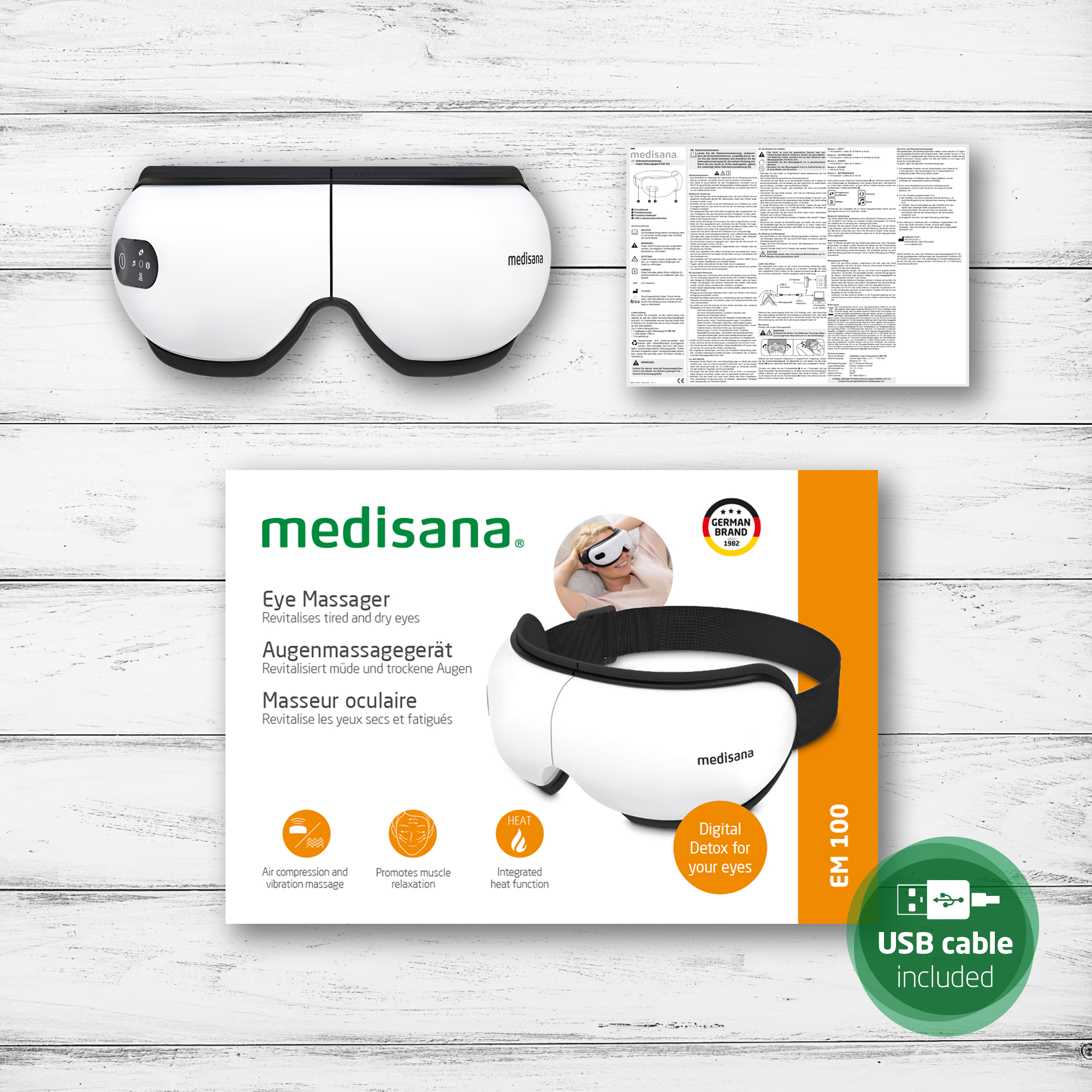 Un masajeador ocular blanco sobre una caja del producto. La caja incluye texto en varios idiomas y un icono de cable USB.