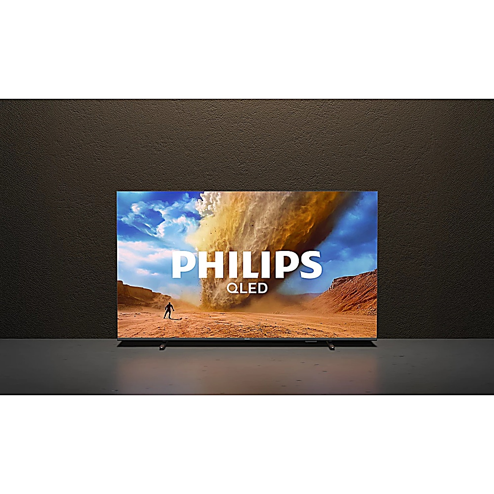Telewizor Philips QLED wyświetla pustynny krajobraz z burzą piaskową i postacią. Tło to teksturowana brązowa ściana.