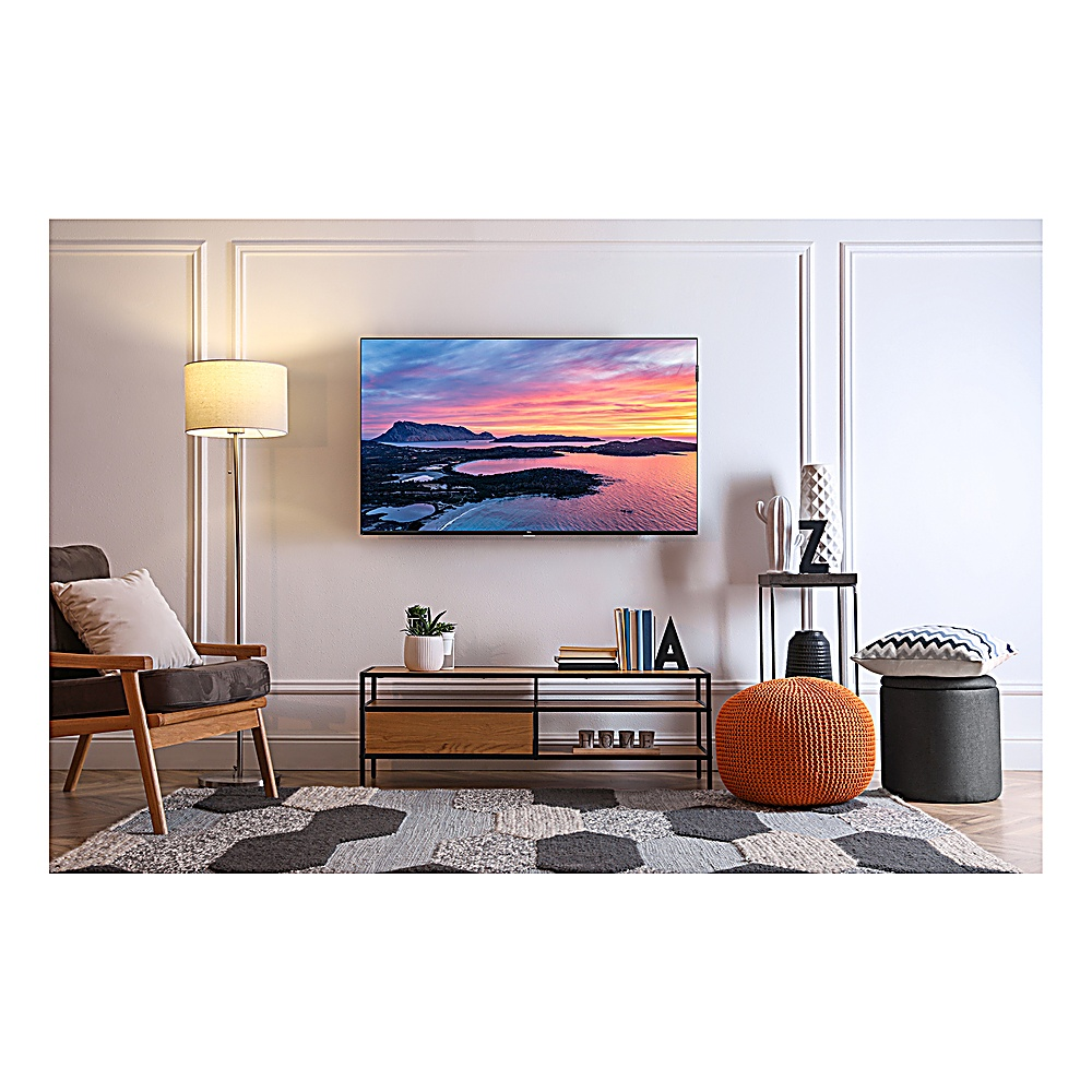 Salon z telewizorem pokazującym zachód słońca nad wodą. Jest sofa, dywan, lampa i elementy dekoracyjne.