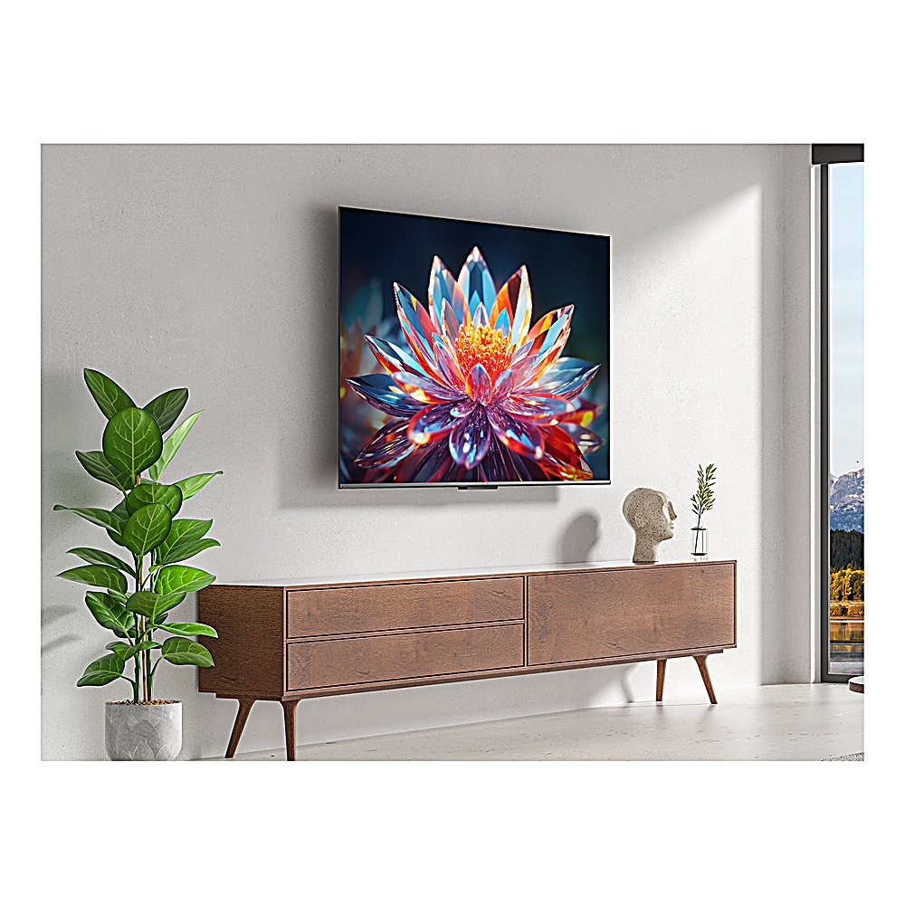 Une télévision affiche une image de fleur colorée. Un meuble en bois, une plante et une sculpture sont devant le mur blanc.