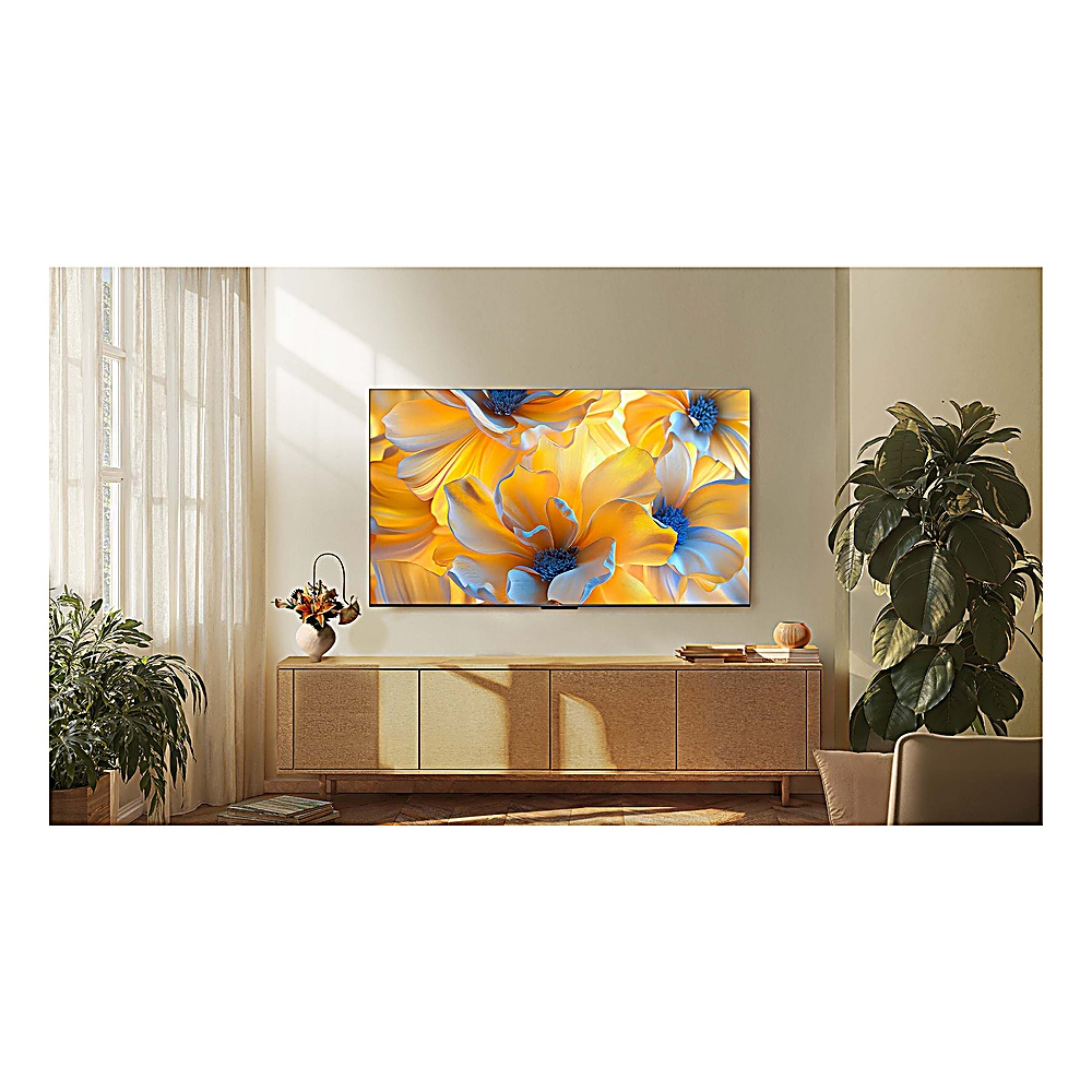 Una grande TV mostra arte floreale. È montata sopra un mobile in legno. Piante e tende incorniciano la scena in un salotto moderno.