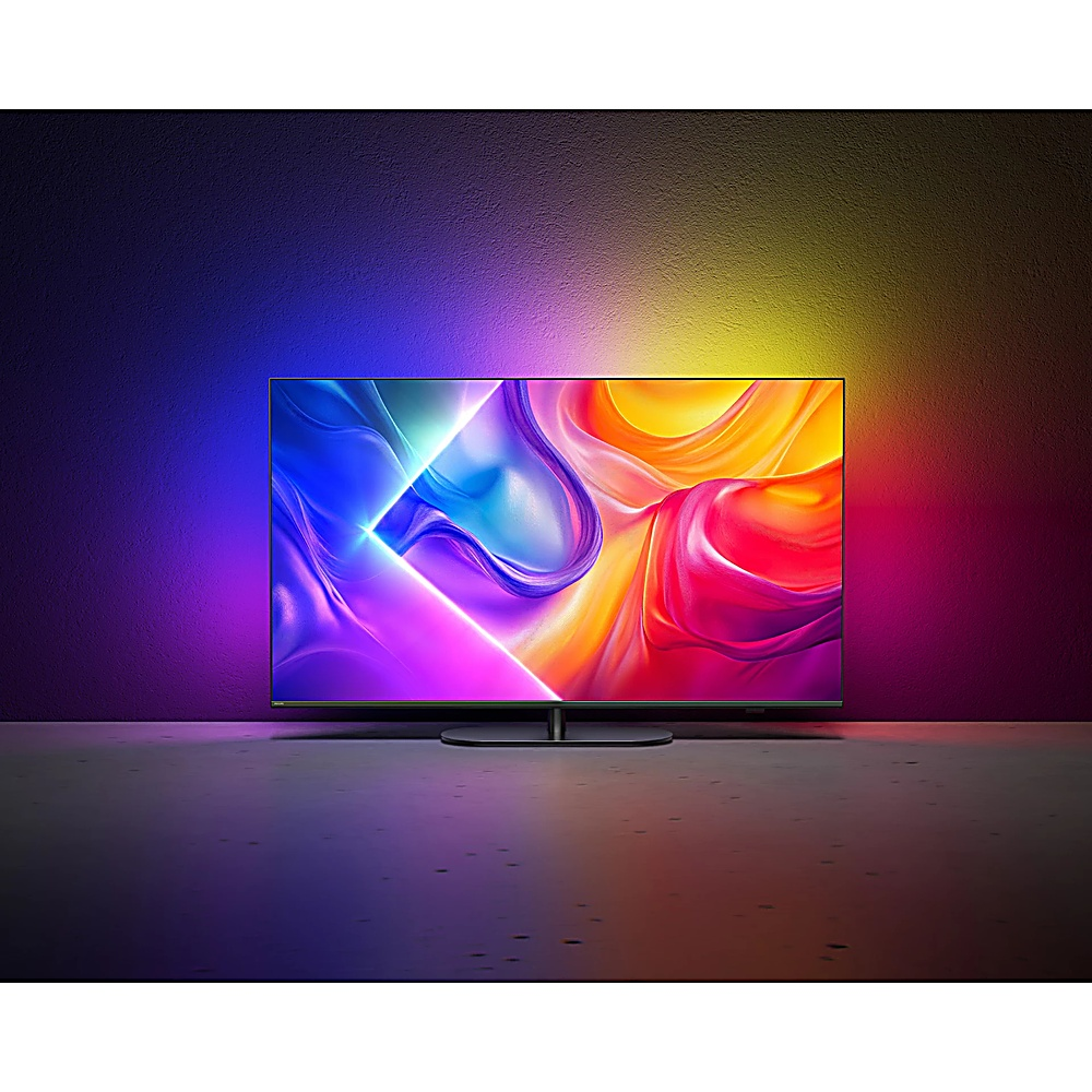 Un grande televisore mostra arte astratta colorata. La parete di sfondo sfuma dal viola al giallo. Il pavimento riflette la luce dello schermo.