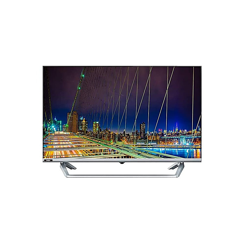Una TV che mostra una scena notturna di una città, con un ponte in primo piano. Gli edifici sono illuminati. La TV ha un supporto argentato.