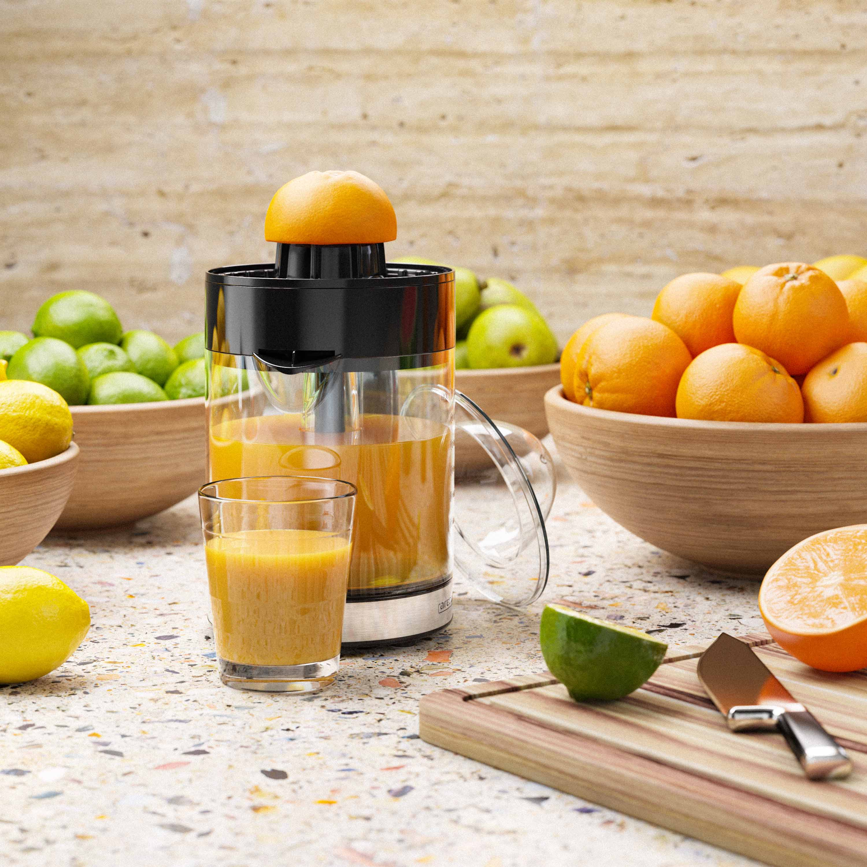 Entsafter mit Orange oben, Glas Saft, Schalen mit Orangen, Zitronen und Limetten auf gefleckter Arbeitsplatte.