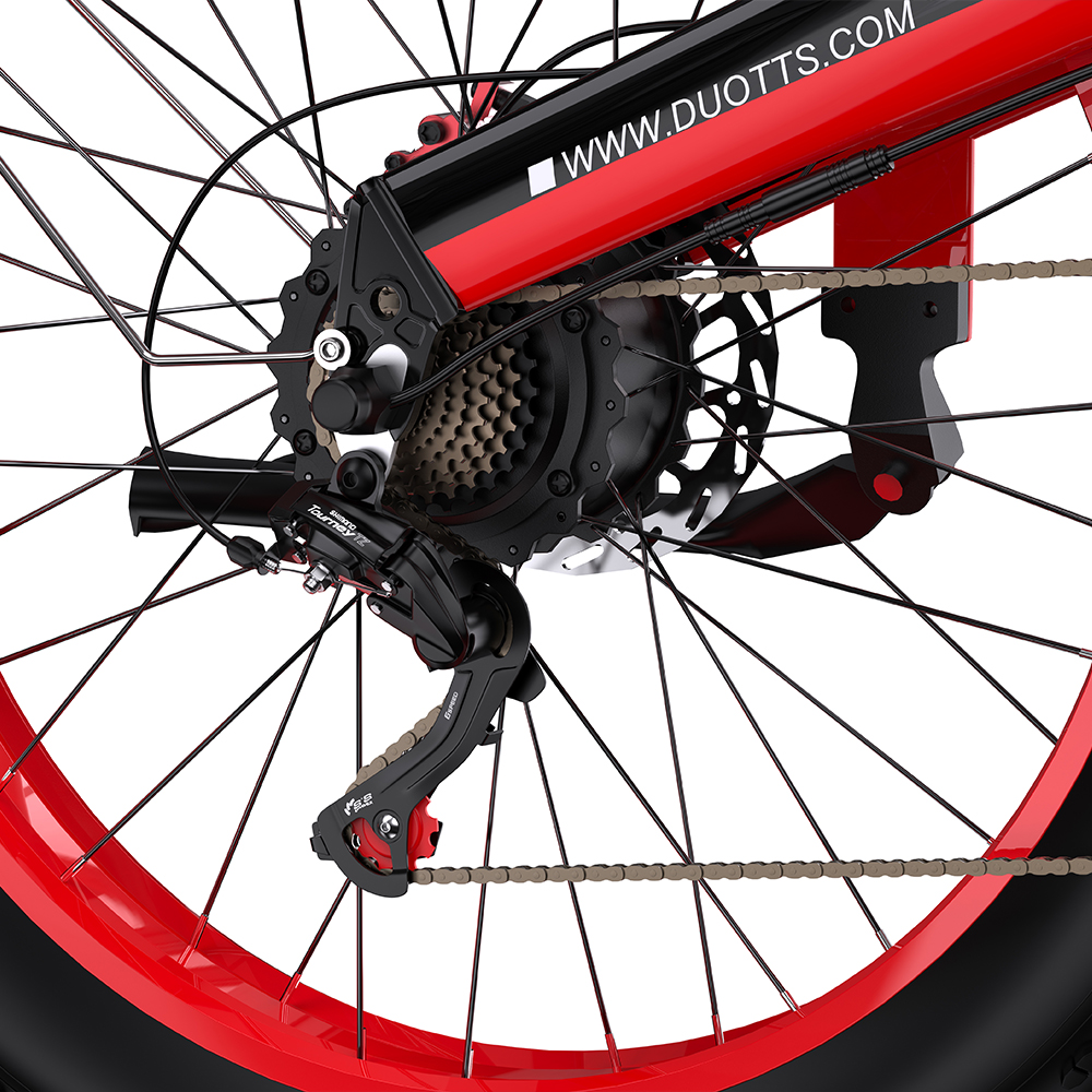 Nahaufnahme eines rot-schwarzen Fahrradrads. Details umfassen Speichen, Zahnräder, Kette und ein Shimano Tourney Schaltwerk.
