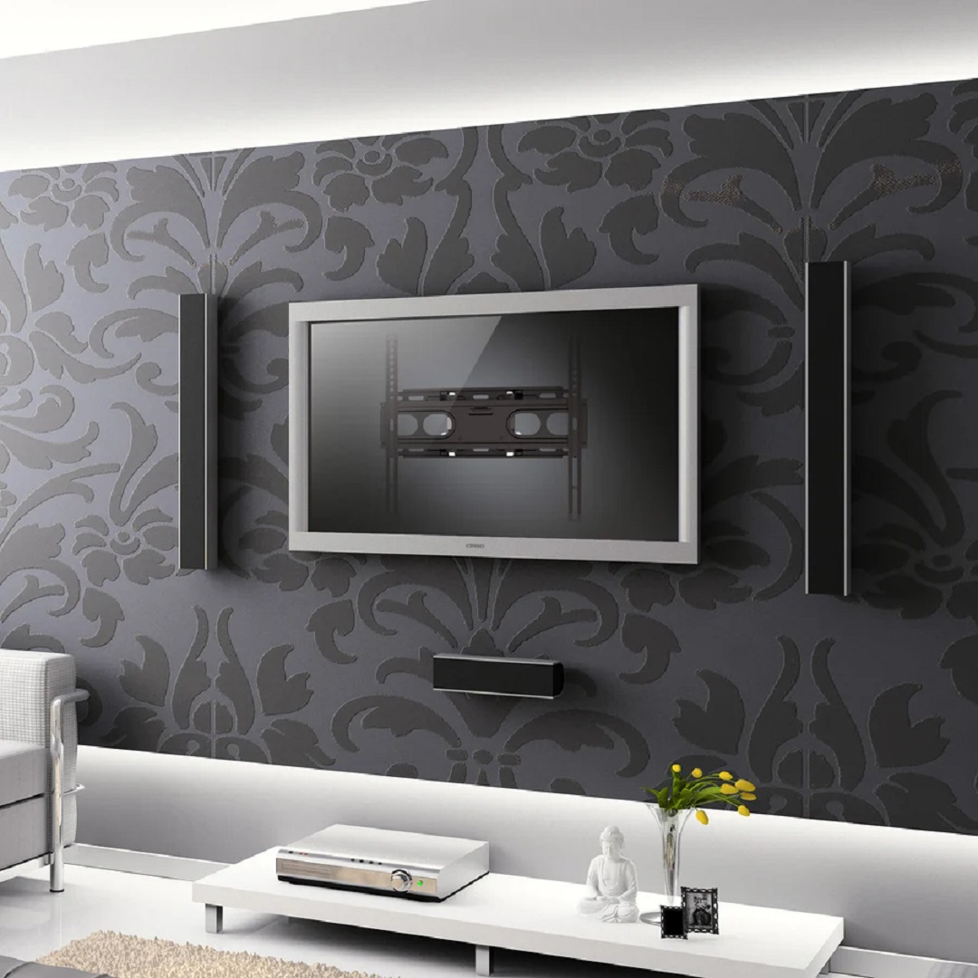 Un televisor montado en una pared estampada. Altavoces a los lados. Mesa blanca con estatua de Buda y flores.