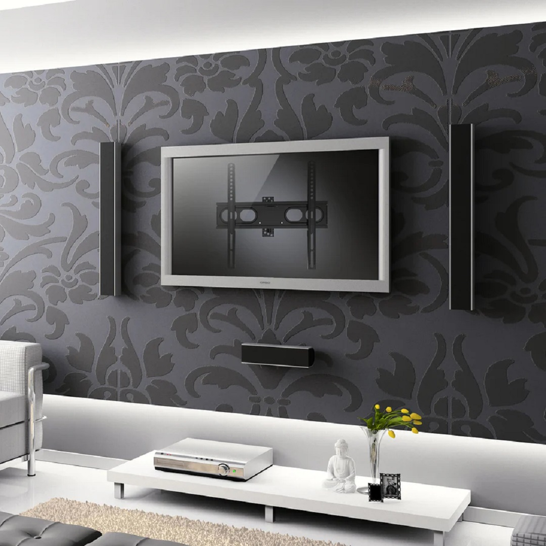Salón: TV en pared estampada, altavoces, mesa blanca con estatua de Buda, reproductor de DVD, jarrón con flores amarillas.