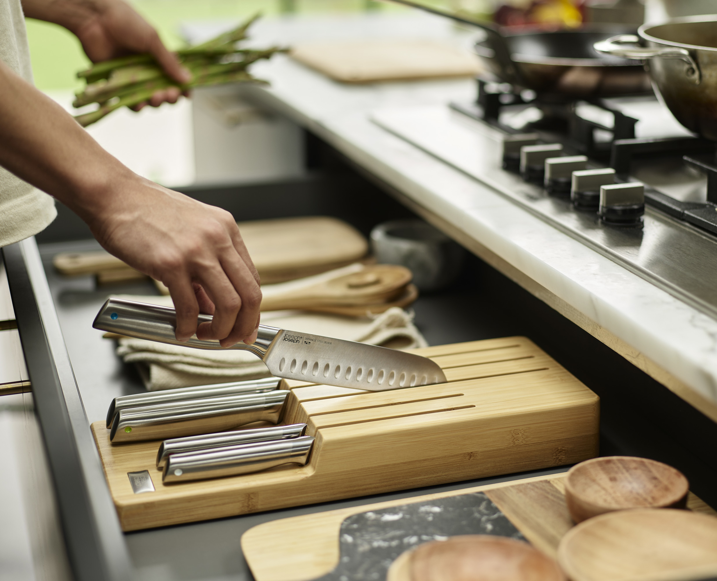 Una persona pone un cuchillo en un soporte de cuchillos de madera. Espárragos en la otra mano. Ambiente de cocina.