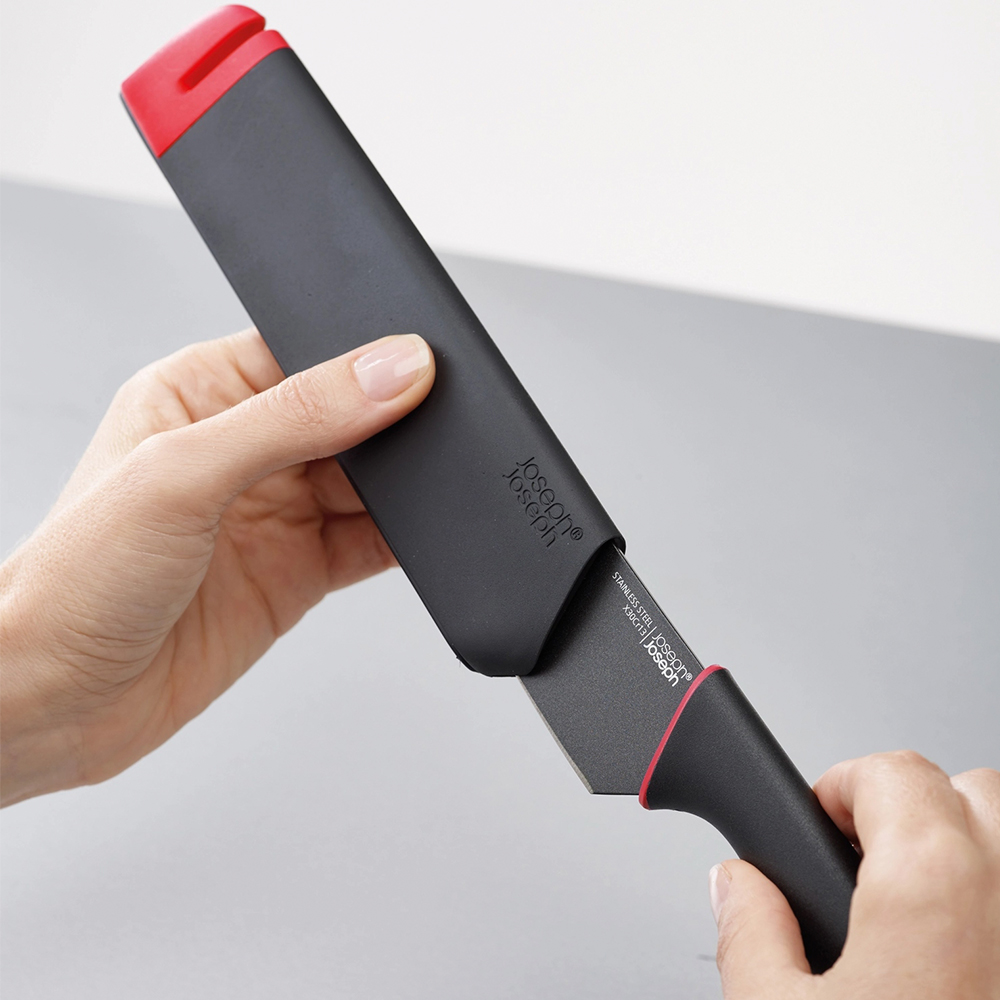 Una persona está sacando un cuchillo negro de su funda negra. El mango y la parte superior de la funda son rojos.