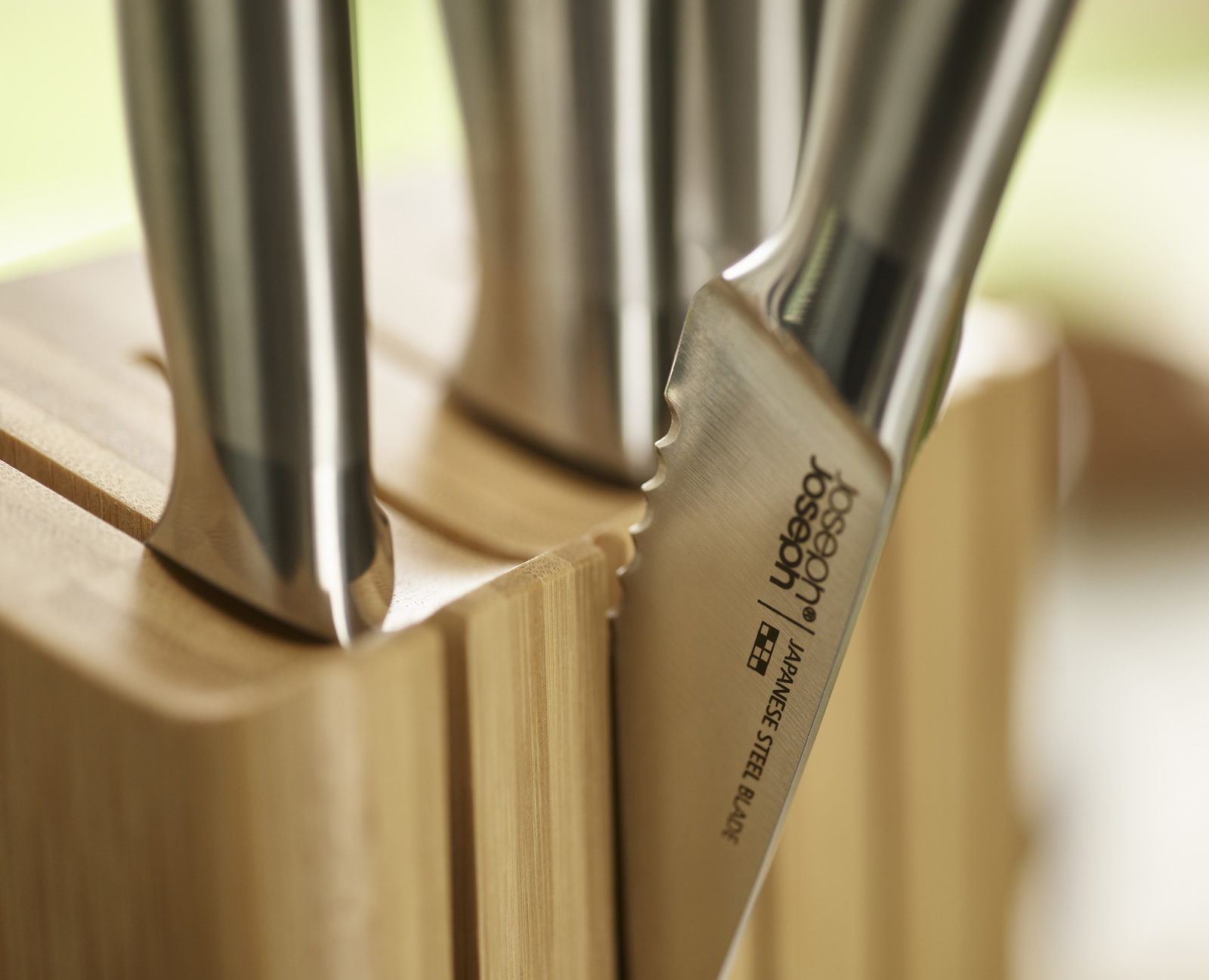 Primer plano de cuchillos en un bloque de madera. Una hoja de cuchillo muestra 'Joseph Joseph' y 'Japanese Steel Blade'.
