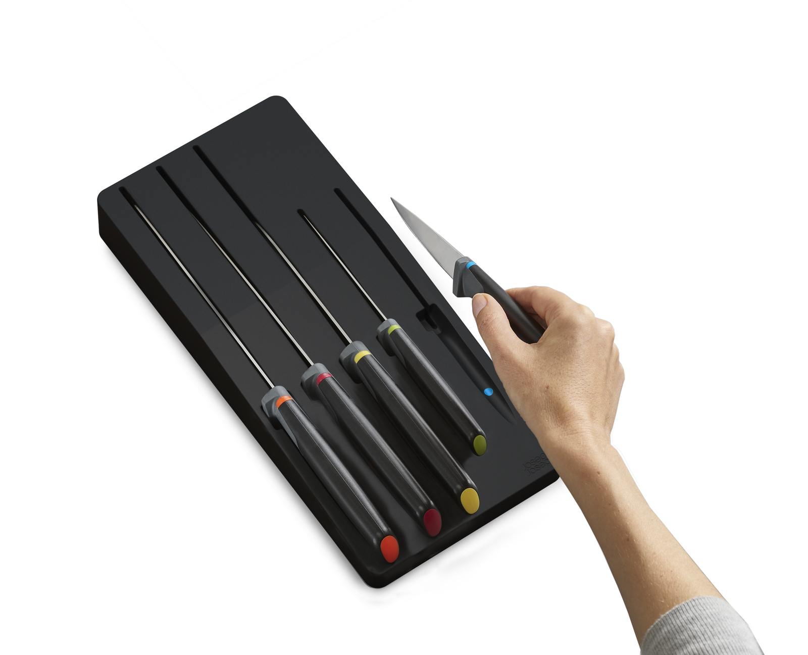 Una mano sosteniendo un cuchillo con mango negro. El cuchillo es parte de un juego en un soporte negro, con extremos de mango de color.