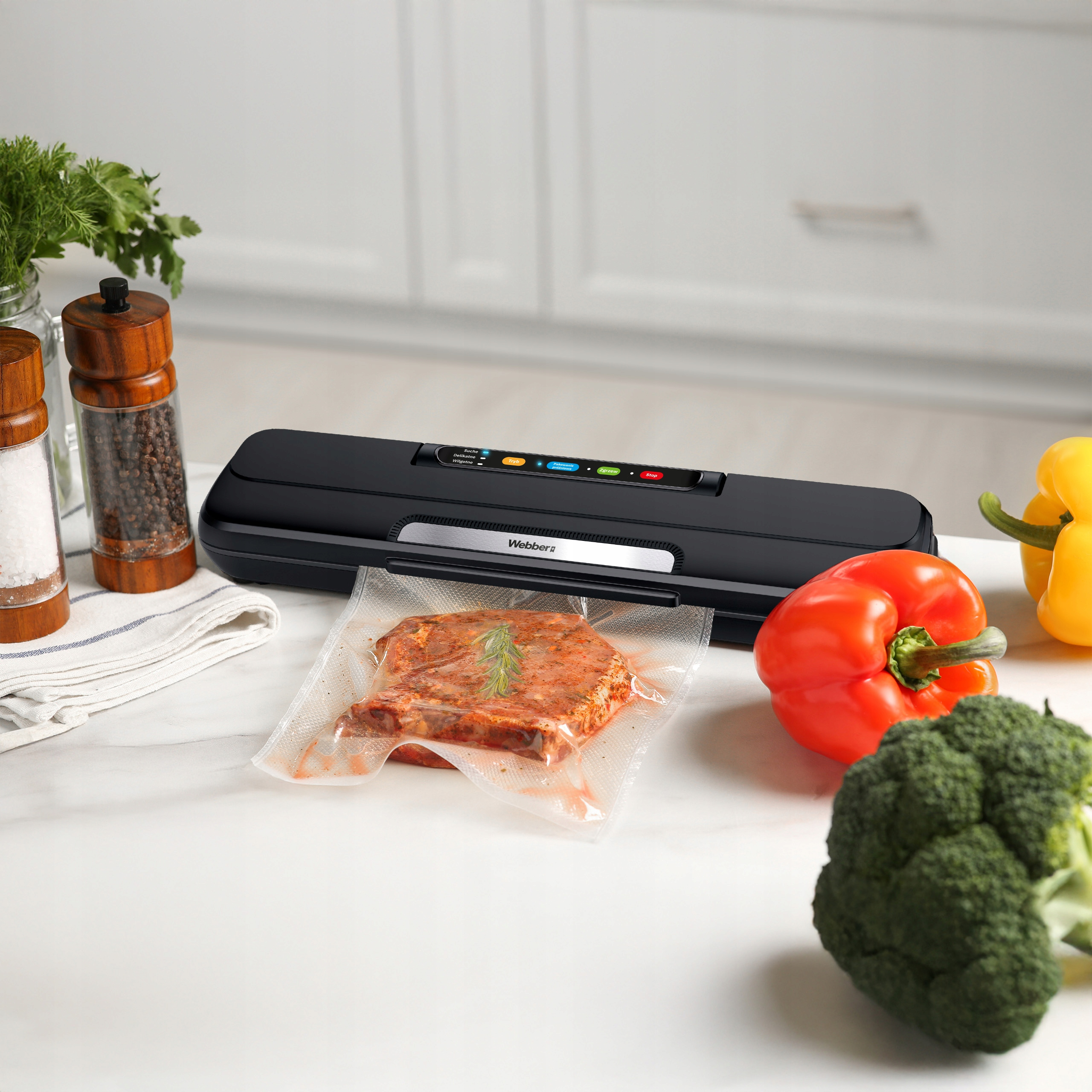 Zgrzewarka próżniowa ze stekiem w worku, czerwoną i żółtą papryką oraz brokułami na białym blacie.