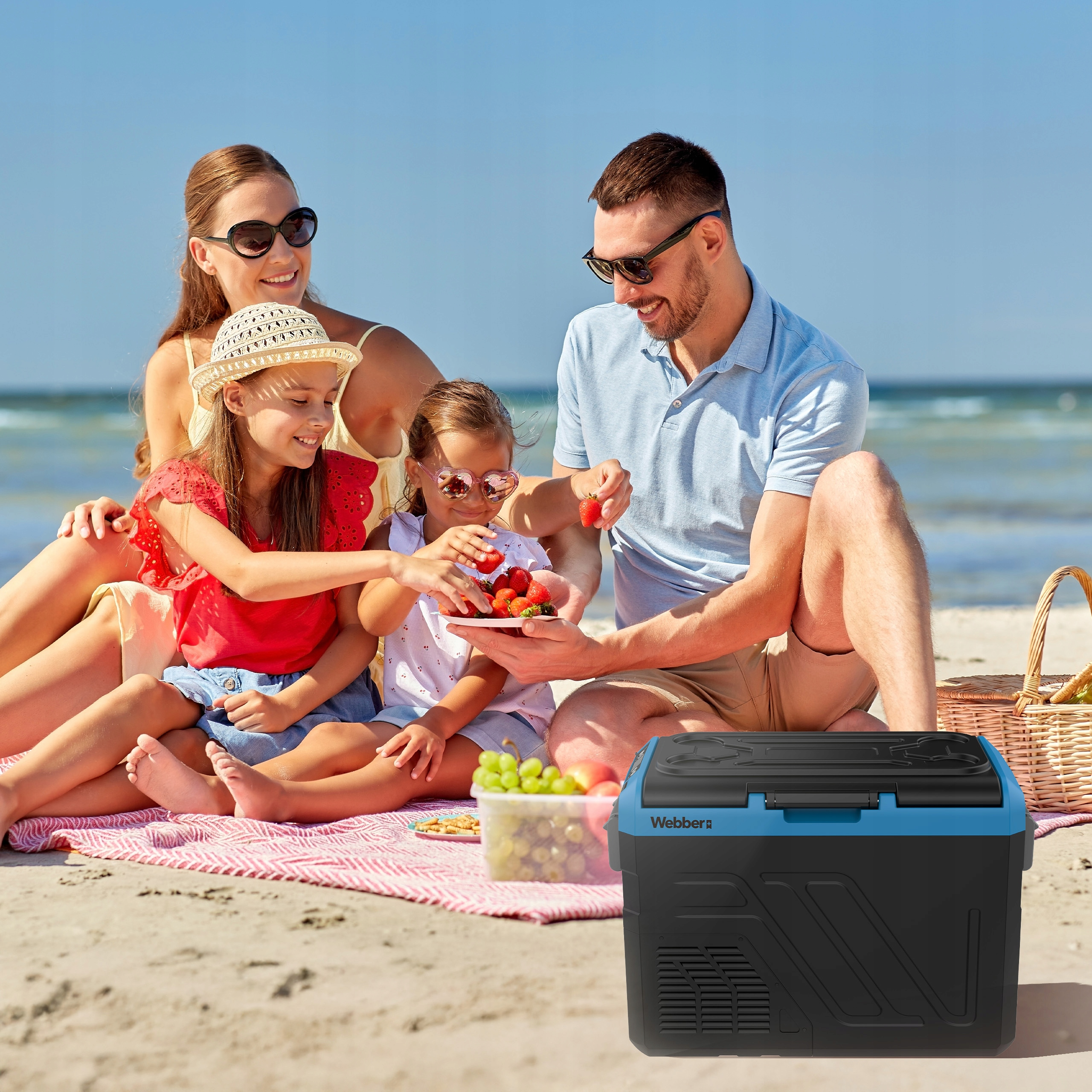 Piknik rodzinny na plaży. Ludzie jedzą truskawki. Chłodziarka jest z przodu.