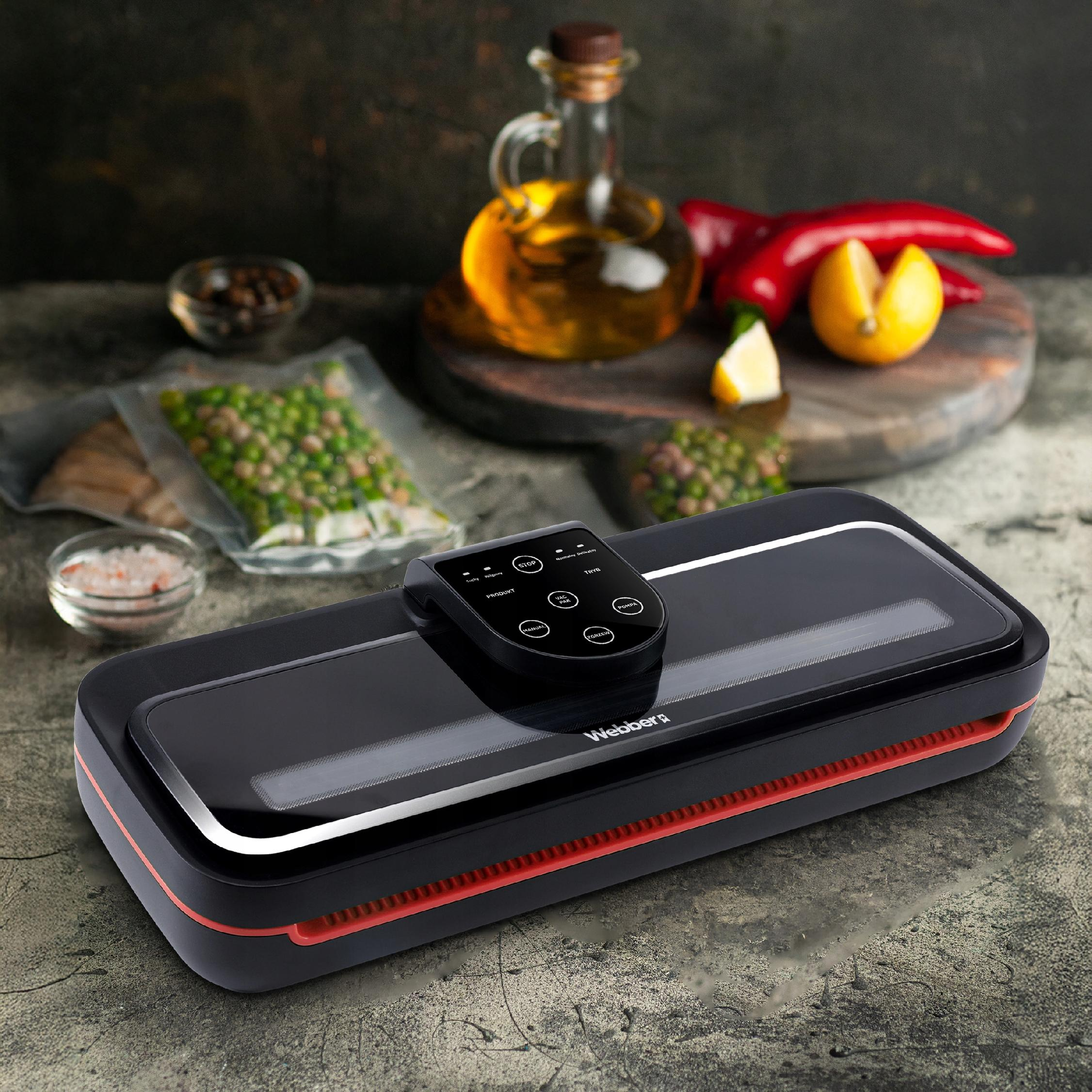 Czarna zgrzewarka do żywności z czarnym panelem sterowania na stole. Różne składniki w tle.