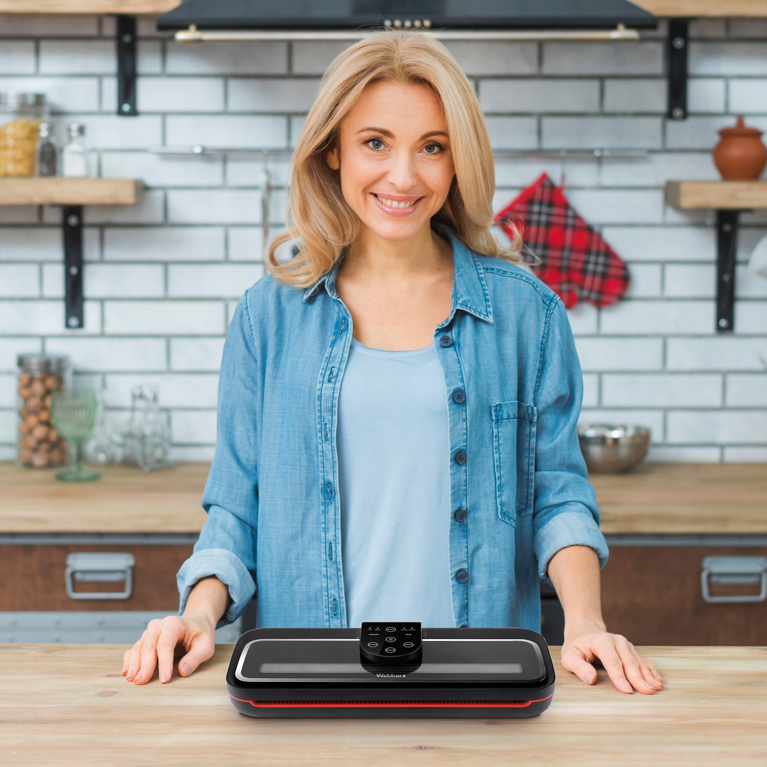Kobieta w kuchni uśmiecha się do kamery. Czarna zgrzewarka do żywności stoi przed nią na stole.