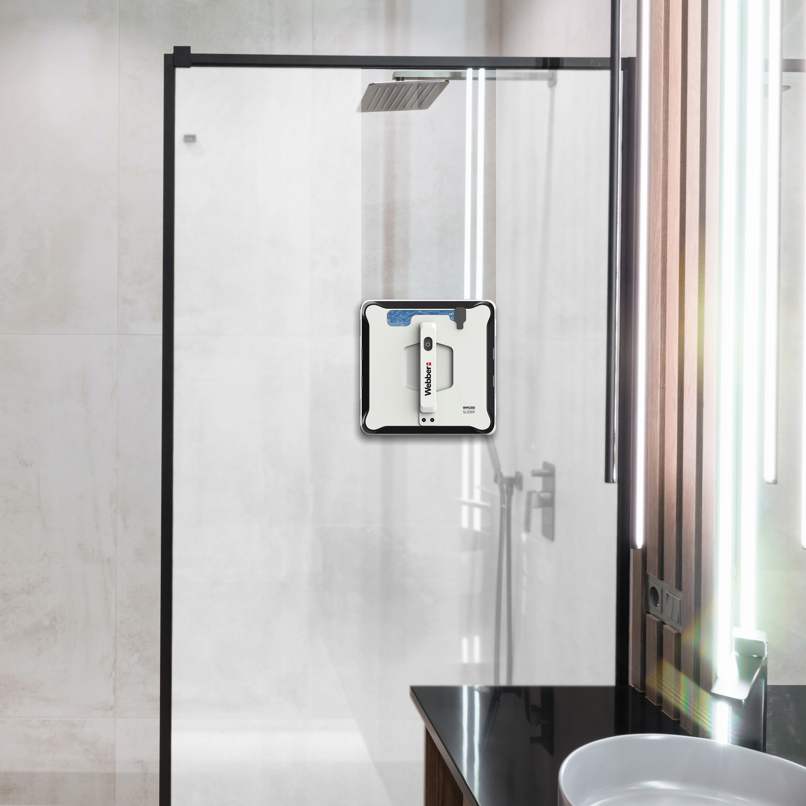 Łazienka z prysznicem i robotem do czyszczenia okien przymocowanym do szyby. Umywalka znajduje się na pierwszym planie.