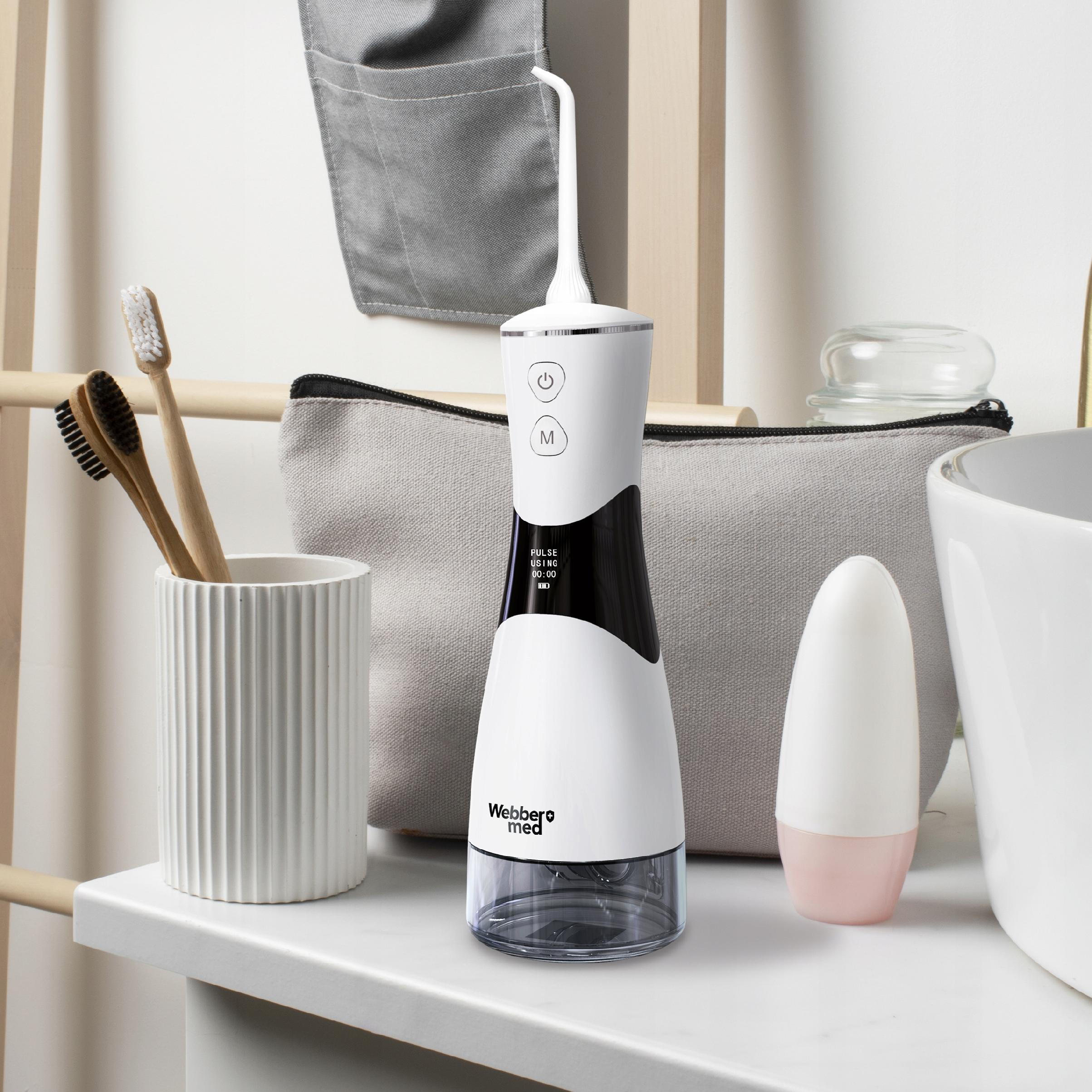 Un idropulsore bianco e nero, spazzolini da denti e un contenitore bianco su una superficie bianca con sfondo grigio.