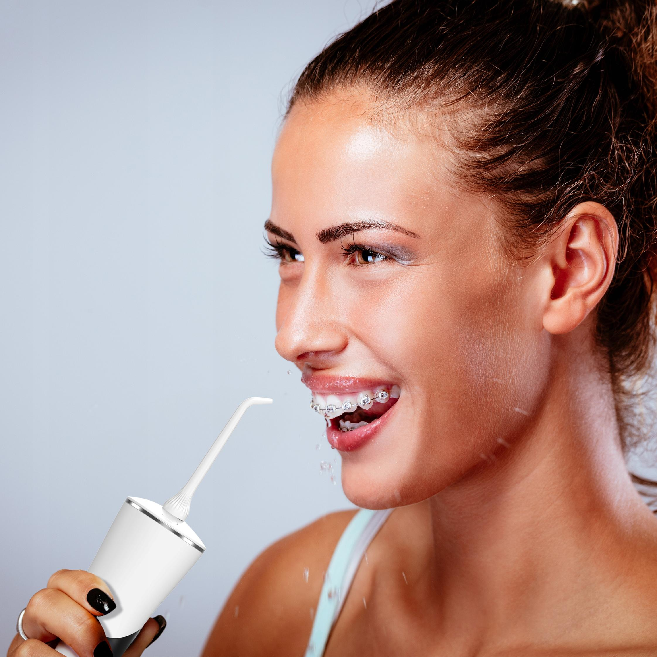Una donna sorride mentre usa un idropulsore bianco. Ha l'apparecchio e lo smalto nero.