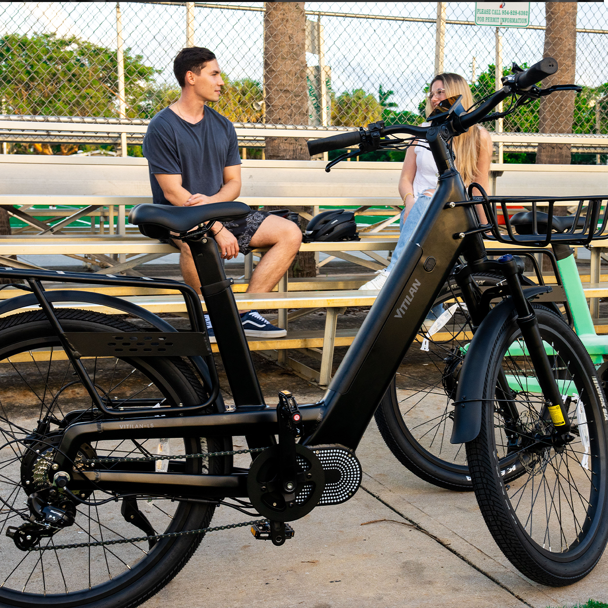 Czarny rower Vitilan na pierwszym planie. Dwie osoby siedzą na ławce w tle. Zielony rower po prawej.
