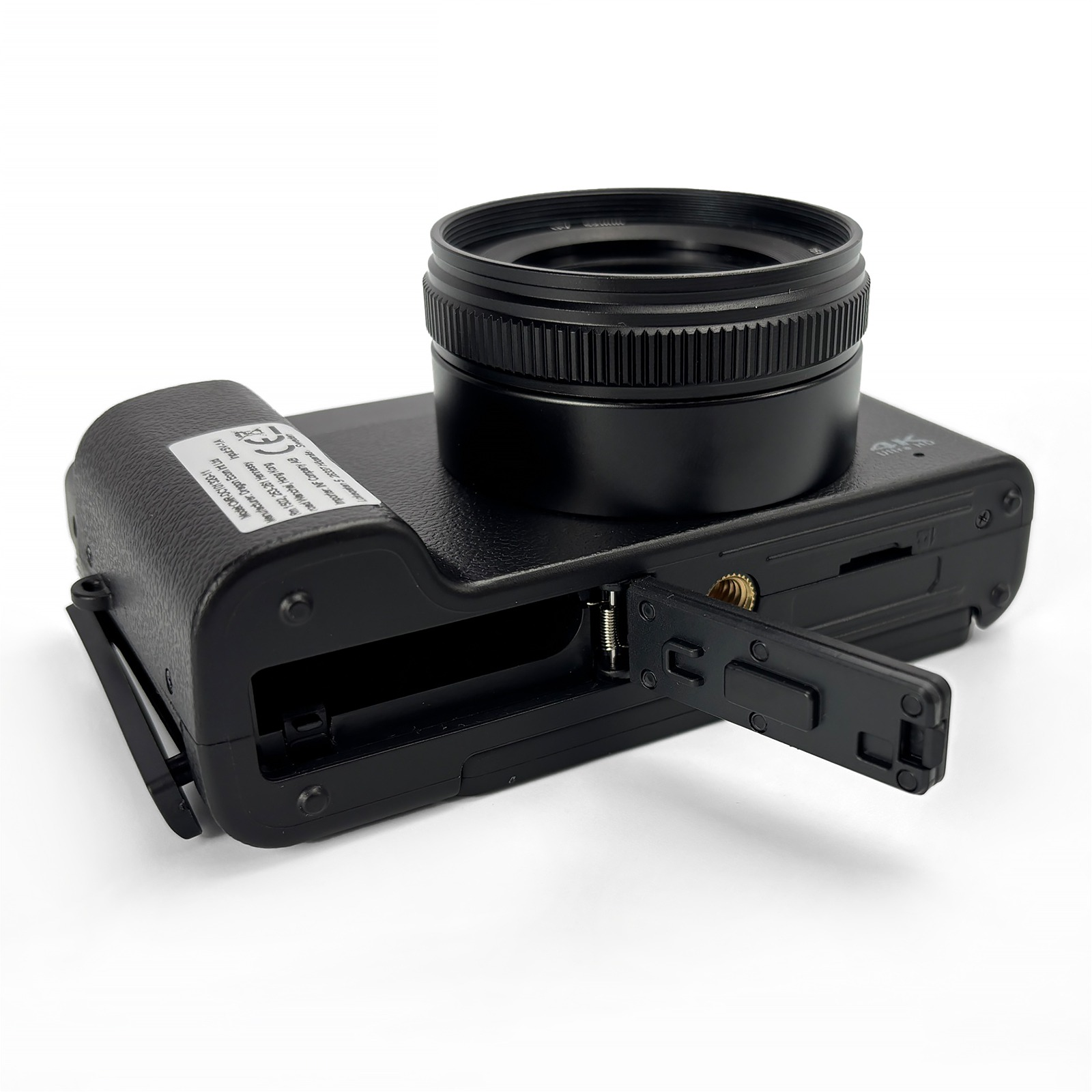 Czarny aparat z dołączonym obiektywem. Drzwiczki baterii są otwarte.