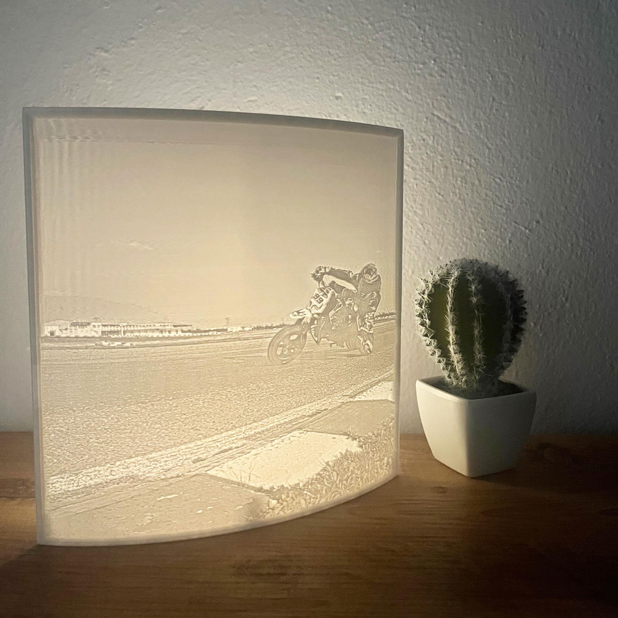 Una lámpara con la imagen de una carrera de motos. Un cactus está al lado de la lámpara sobre una superficie de madera.