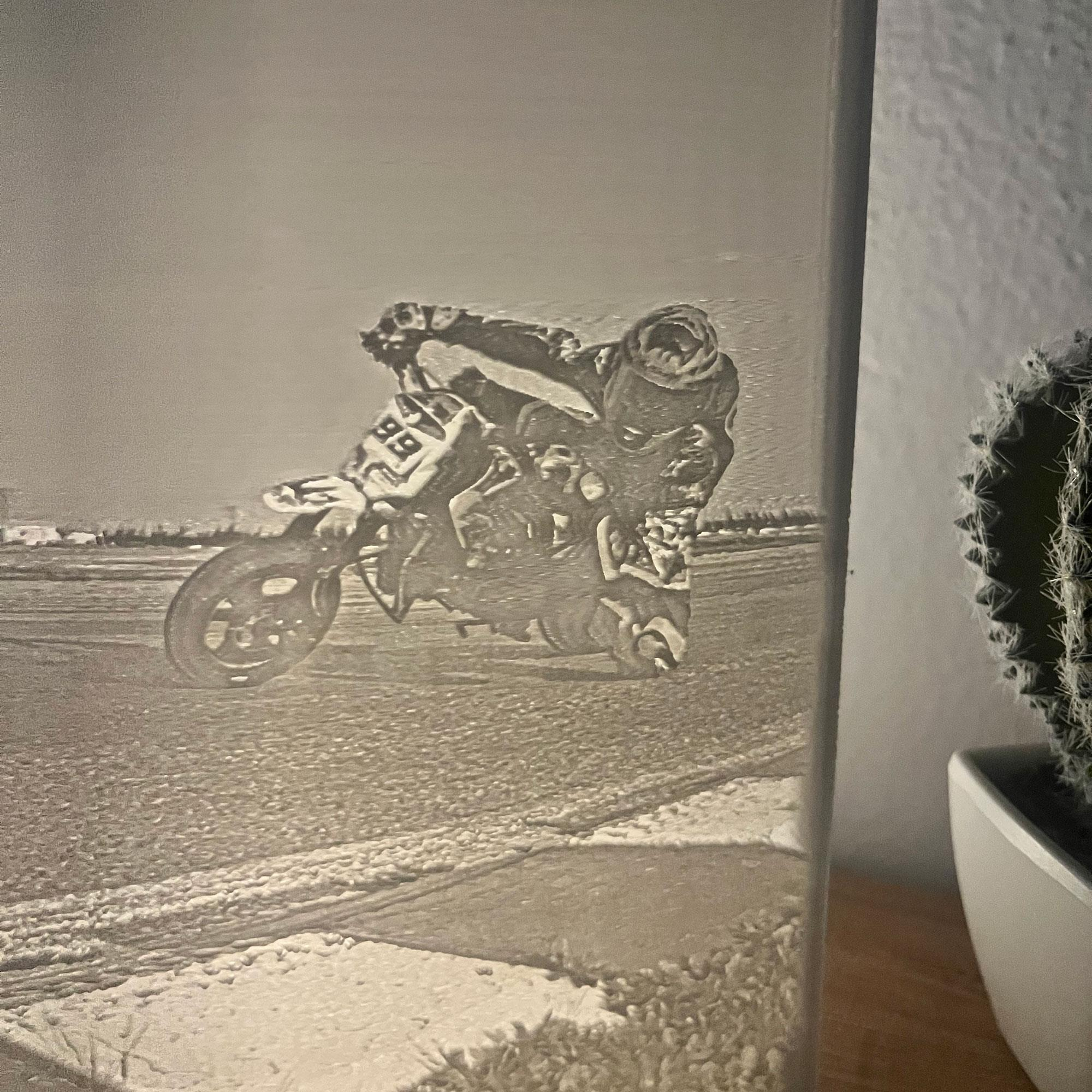 Un motociclista se inclina en una curva en una pista. La imagen es un dibujo en escala de grises en una pared, con un cactus.