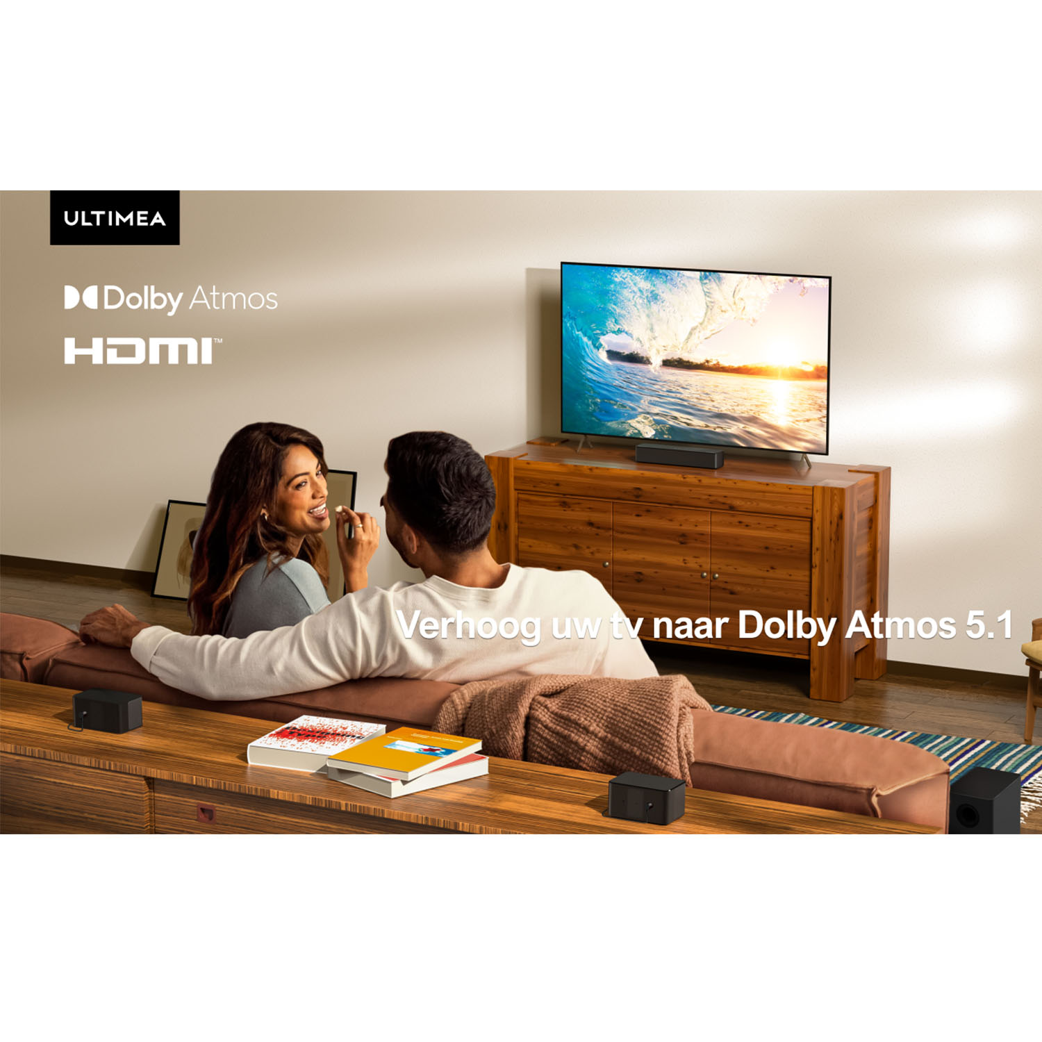 Een stel zit op een bank en kijkt tv. De tv toont een golf die breekt. Luidsprekers zijn door de kamer geplaatst.