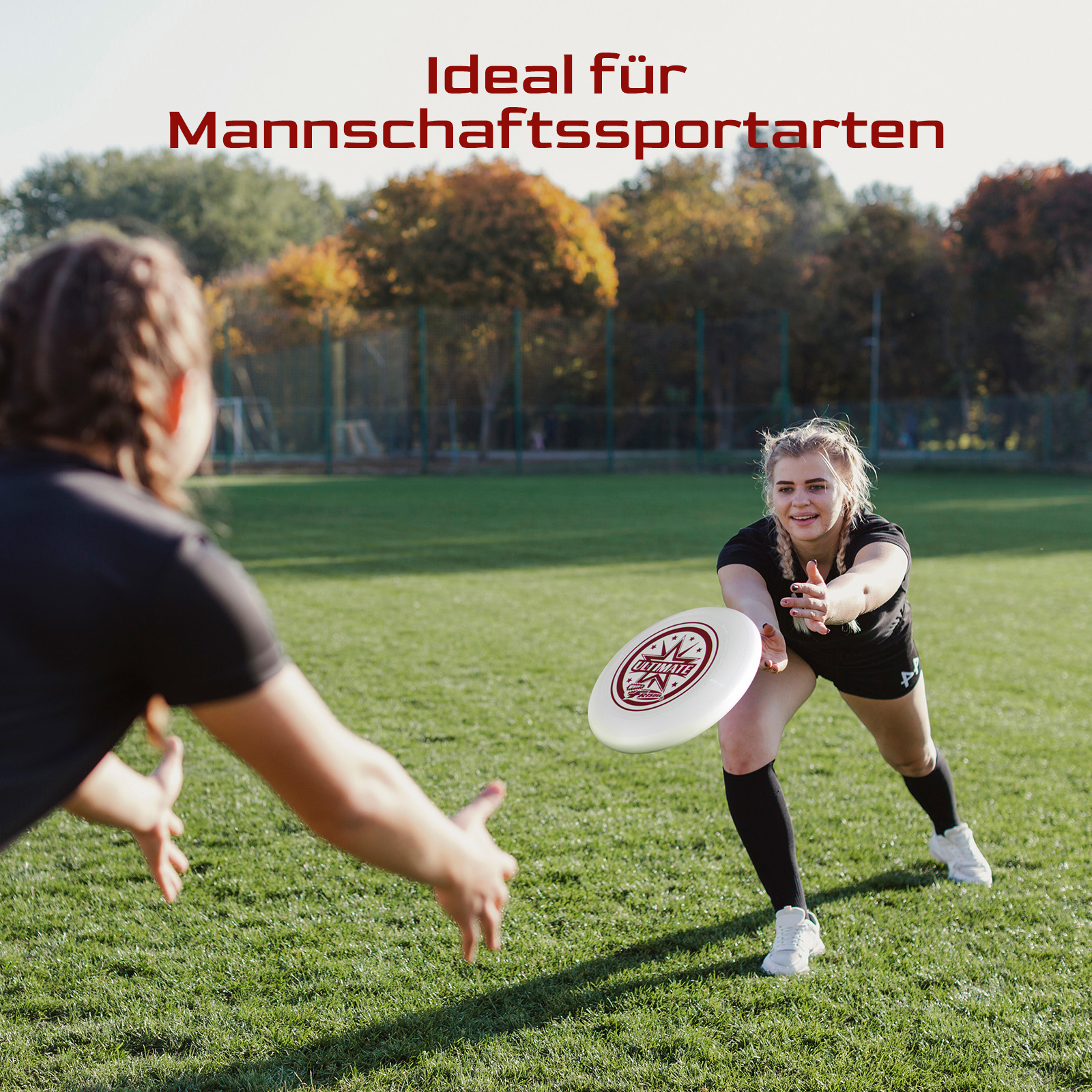 Zwei Frauen spielen Frisbee auf einem grünen Feld. Eine wirft, die andere greift danach.