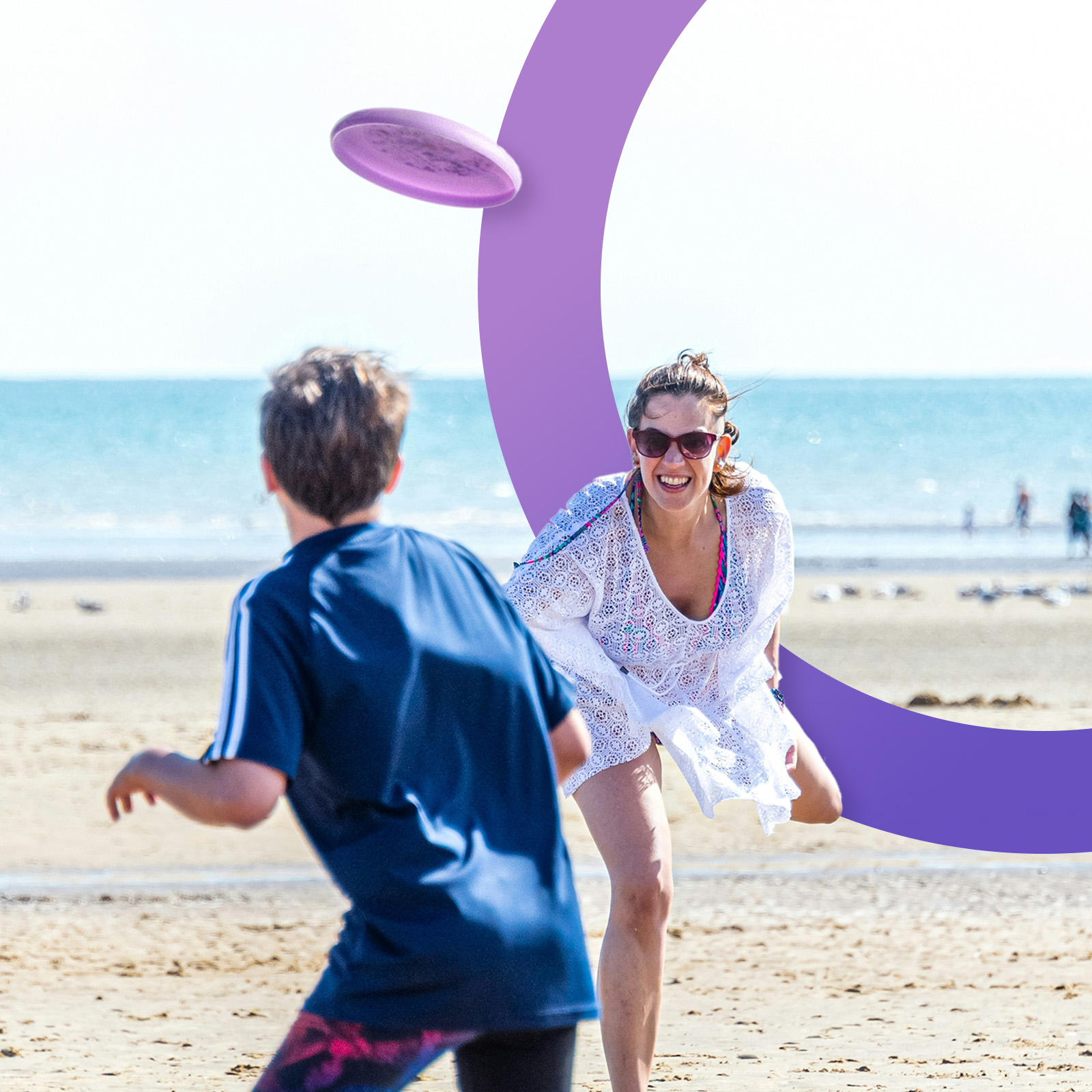 Frau und Junge spielen am Strand Frisbee. Lila Frisbee in der Luft. Klarer Himmel und Meer im Hintergrund.