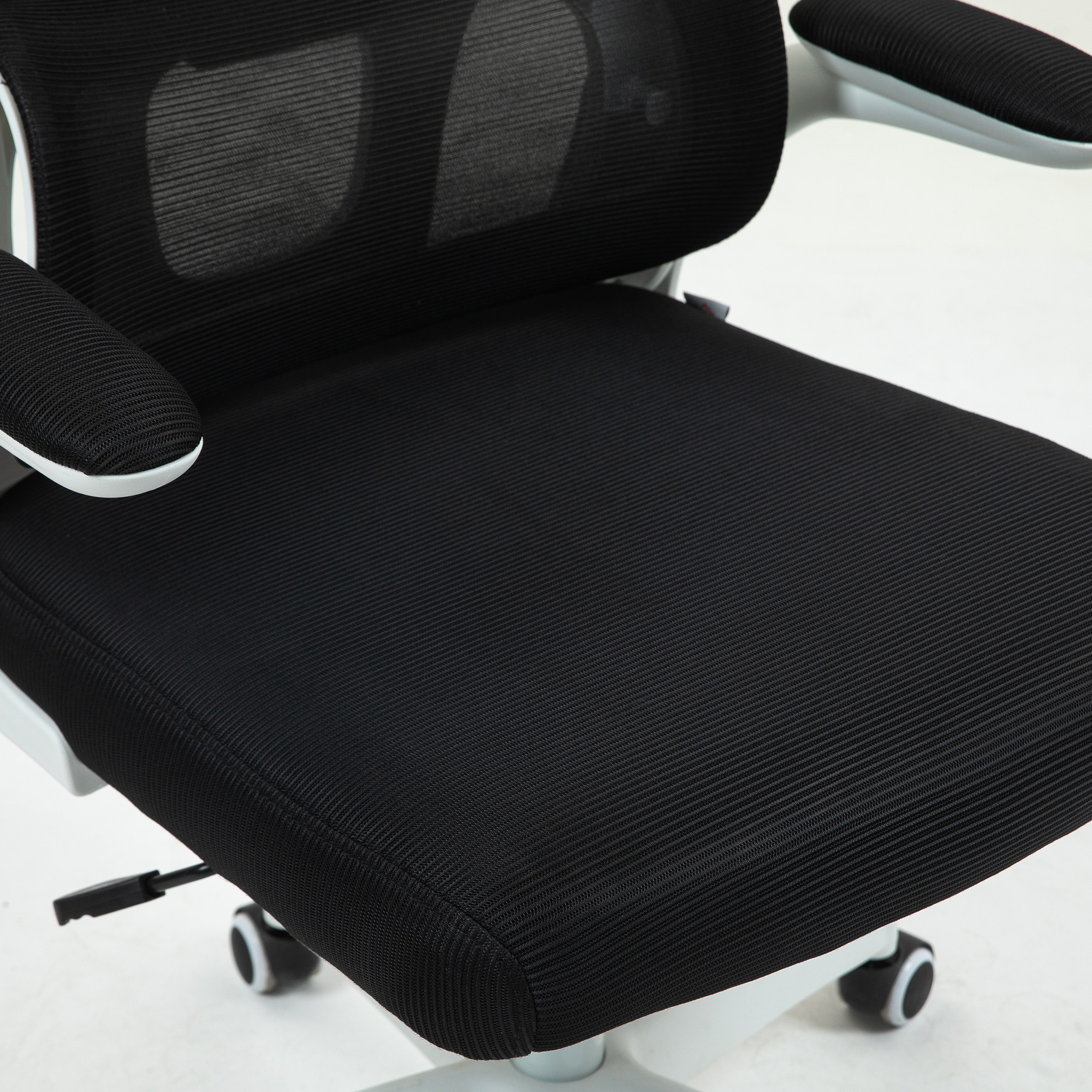 Primo piano di una sedia da ufficio nera. Ha schienale e seduta in rete, con braccioli e base bianchi. Lo sfondo è bianco.