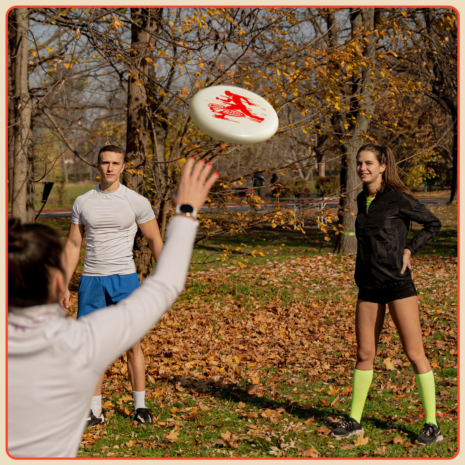 Leute spielen Frisbee im Park. Eine Person wirft die Frisbeescheibe. Andere sind bereit, sie zu fangen. Herbstblätter liegen am Boden.