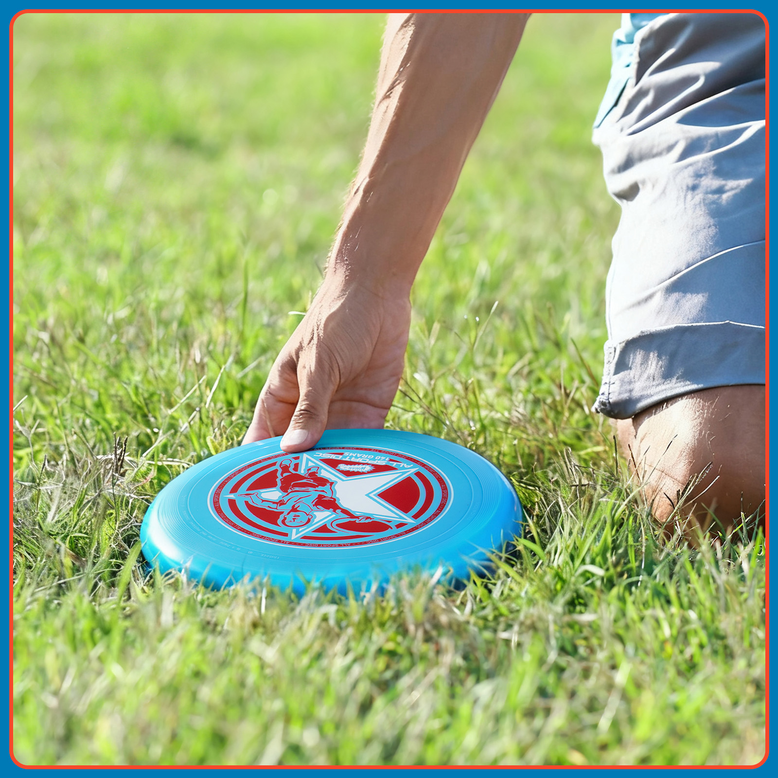 Die Hand einer Person ist in der Nähe einer blauen Frisbeescheibe auf Gras. Die Frisbeescheibe hat ein rotes Design.