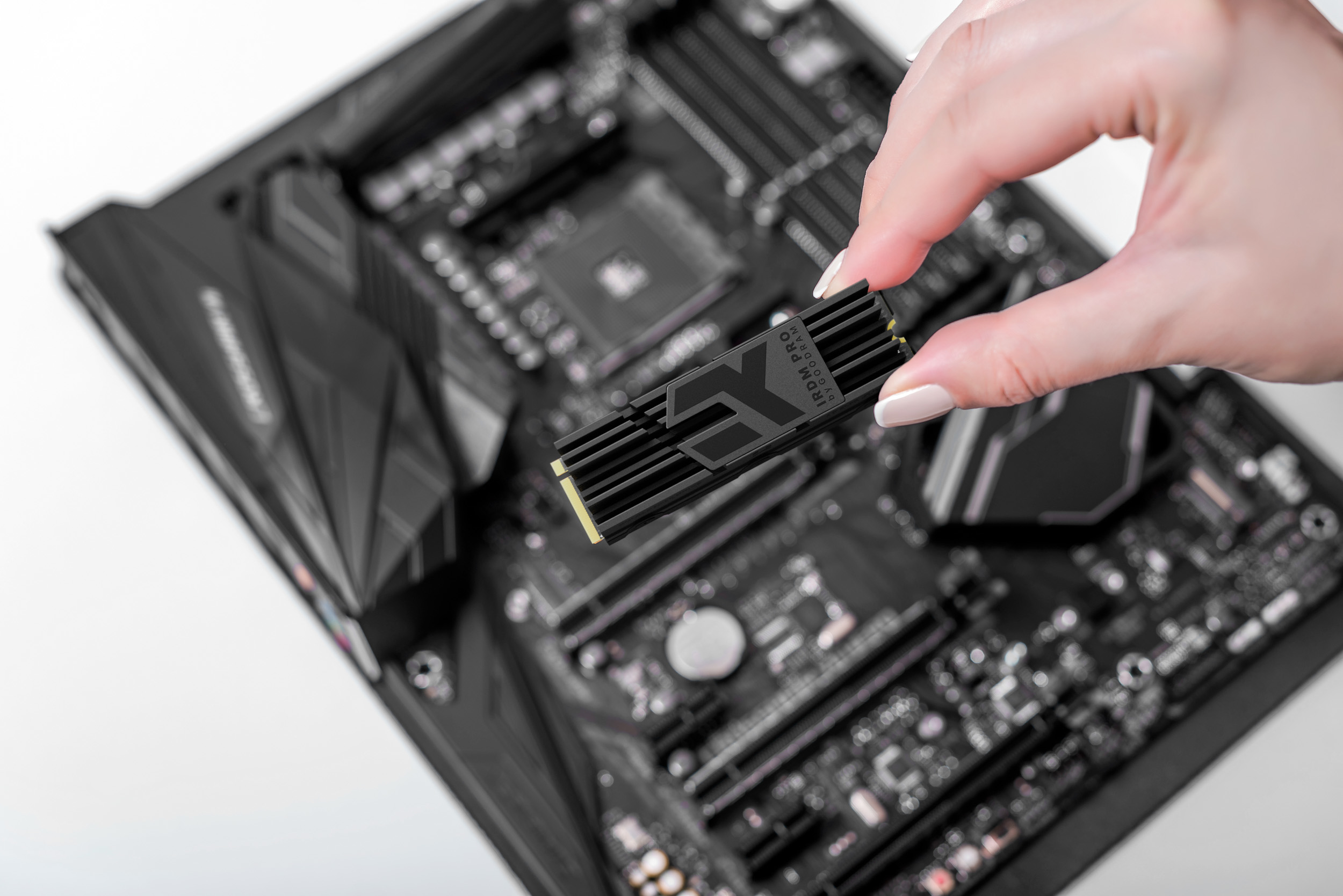 Hand holding a black SSD card over a black motherboard. The card is labeled IRDM PRO. The background is white.