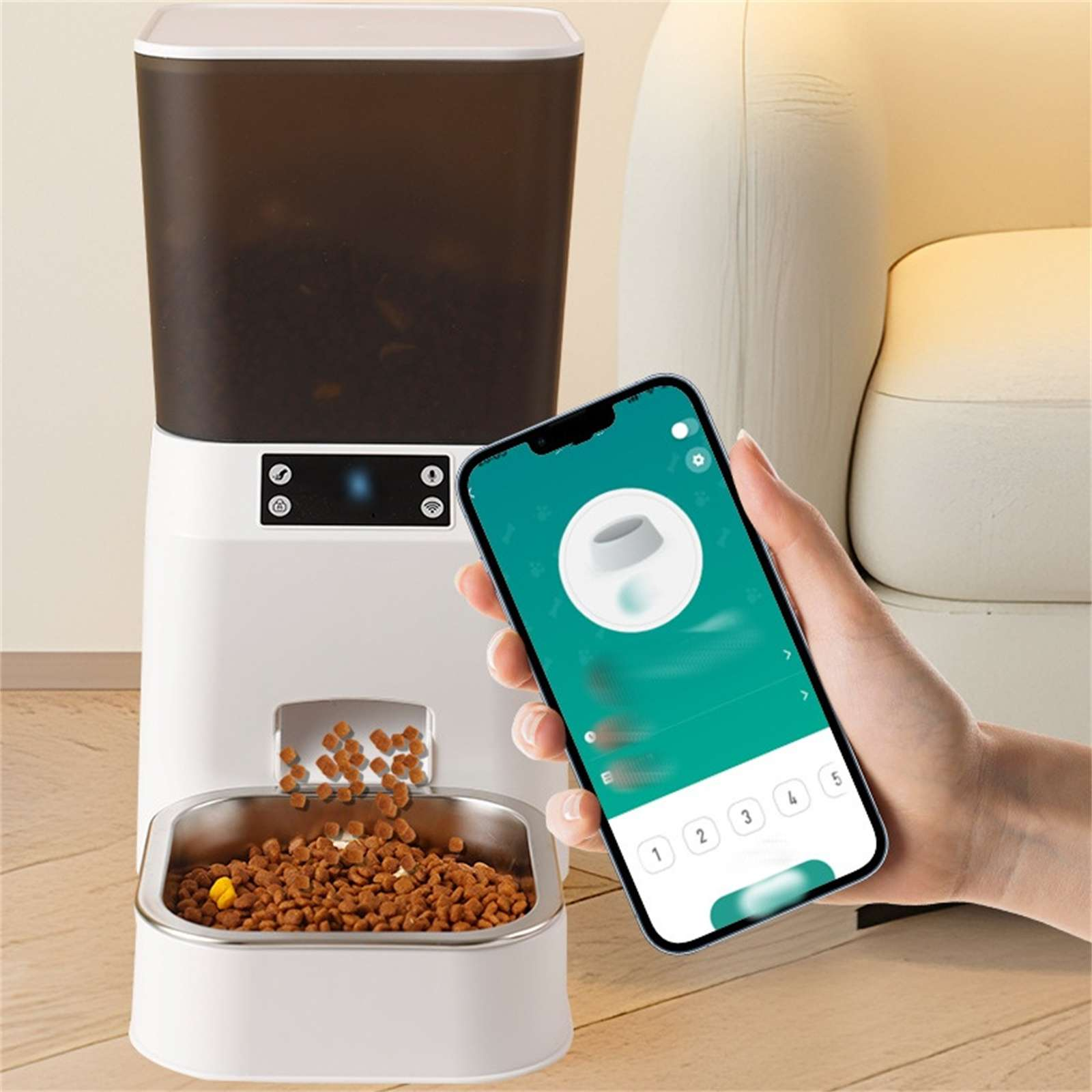 Ein weißer Futterautomat gibt Futter aus. Eine Hand hält ein Telefon mit einer Haustierfutter-App. Hintergrund: eine Couch und Holzboden.