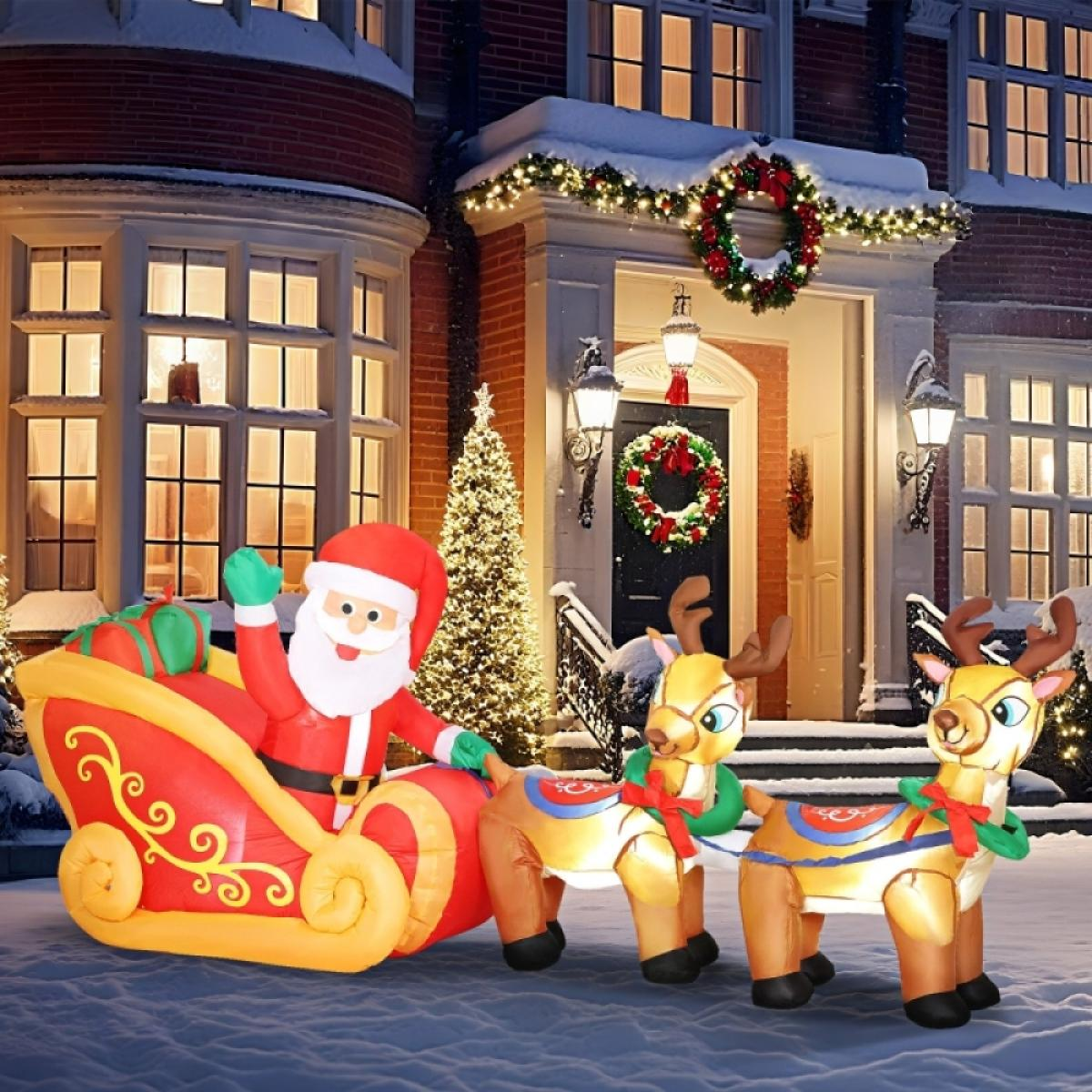 Ein aufblasbarer Weihnachtsmann in einem Schlitten, der von zwei Rentieren gezogen wird, vor einem weihnachtlich geschmückten Haus.