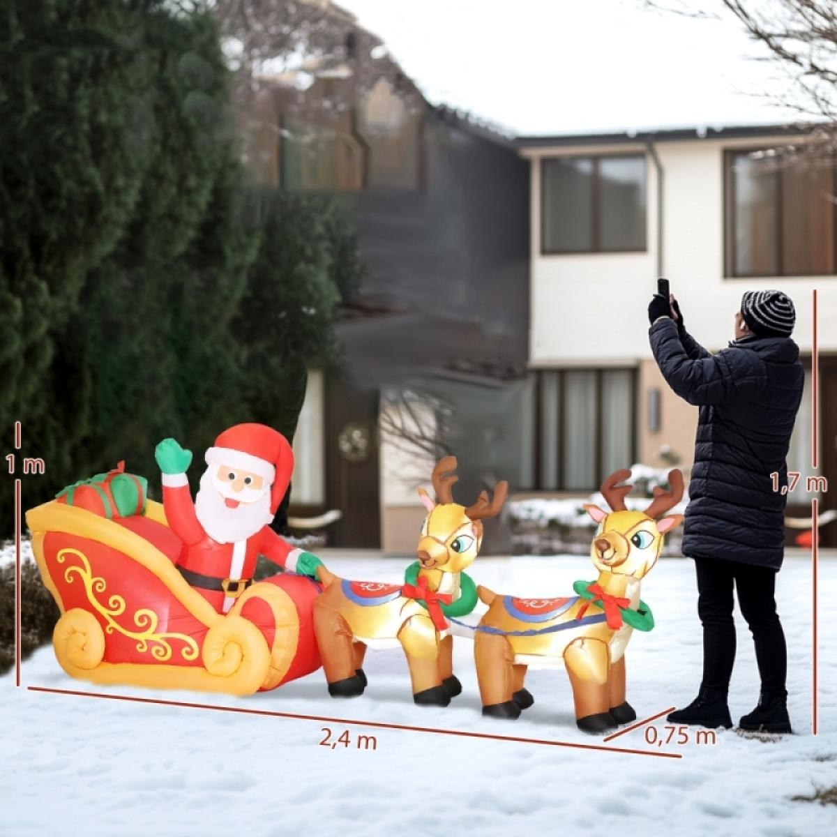 Aufblasbarer Weihnachtsmann in einem Schlitten, der von Rentieren im Schnee gezogen wird. Eine Person macht ein Foto vor einem Haus.