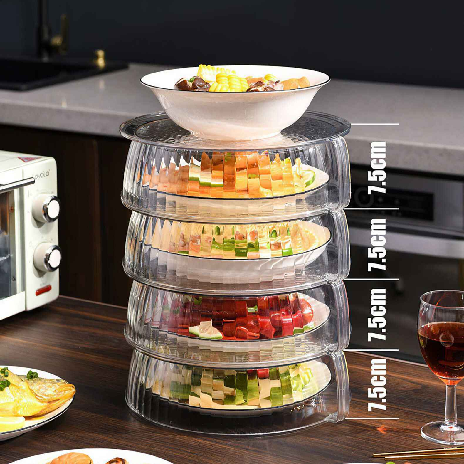 Gestapelte Glasservierschalen mit Essen. Enthält Gemüse, Obst und Mais. Daneben steht ein Weinglas.