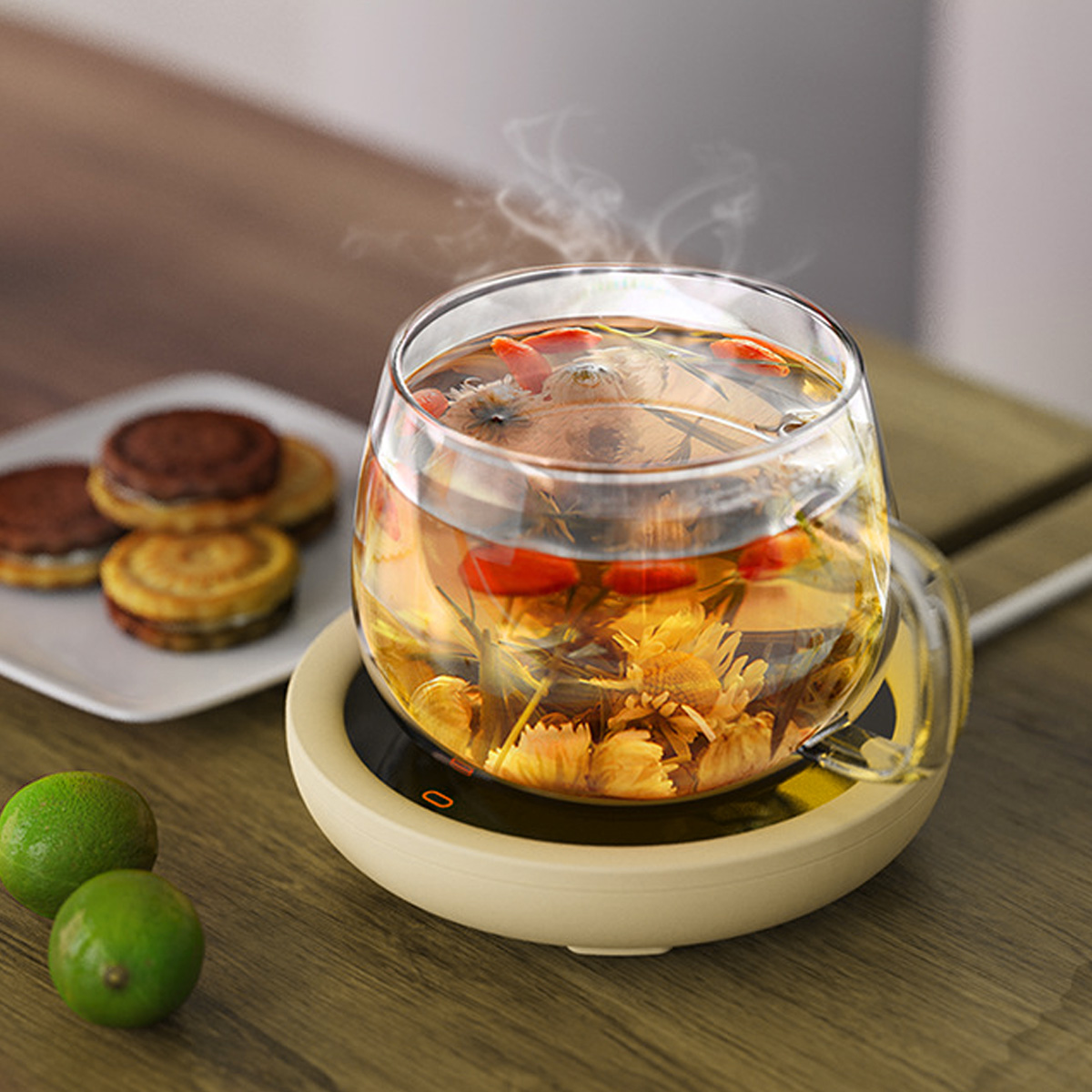 Ein Glas Tee mit Blumen und Früchten steht auf einem Wärmer. Limetten und Kekse stehen auf einem Holztisch.