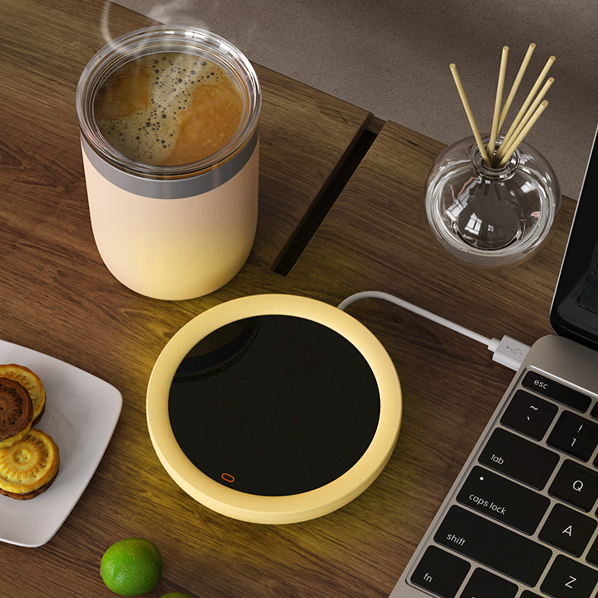 Auf einem Holztisch befinden sich eine Kaffeetasse, ein Wärmer und ein Laptop. Kekse und Limetten sind ebenfalls vorhanden. Ein Diffusor steht daneben.