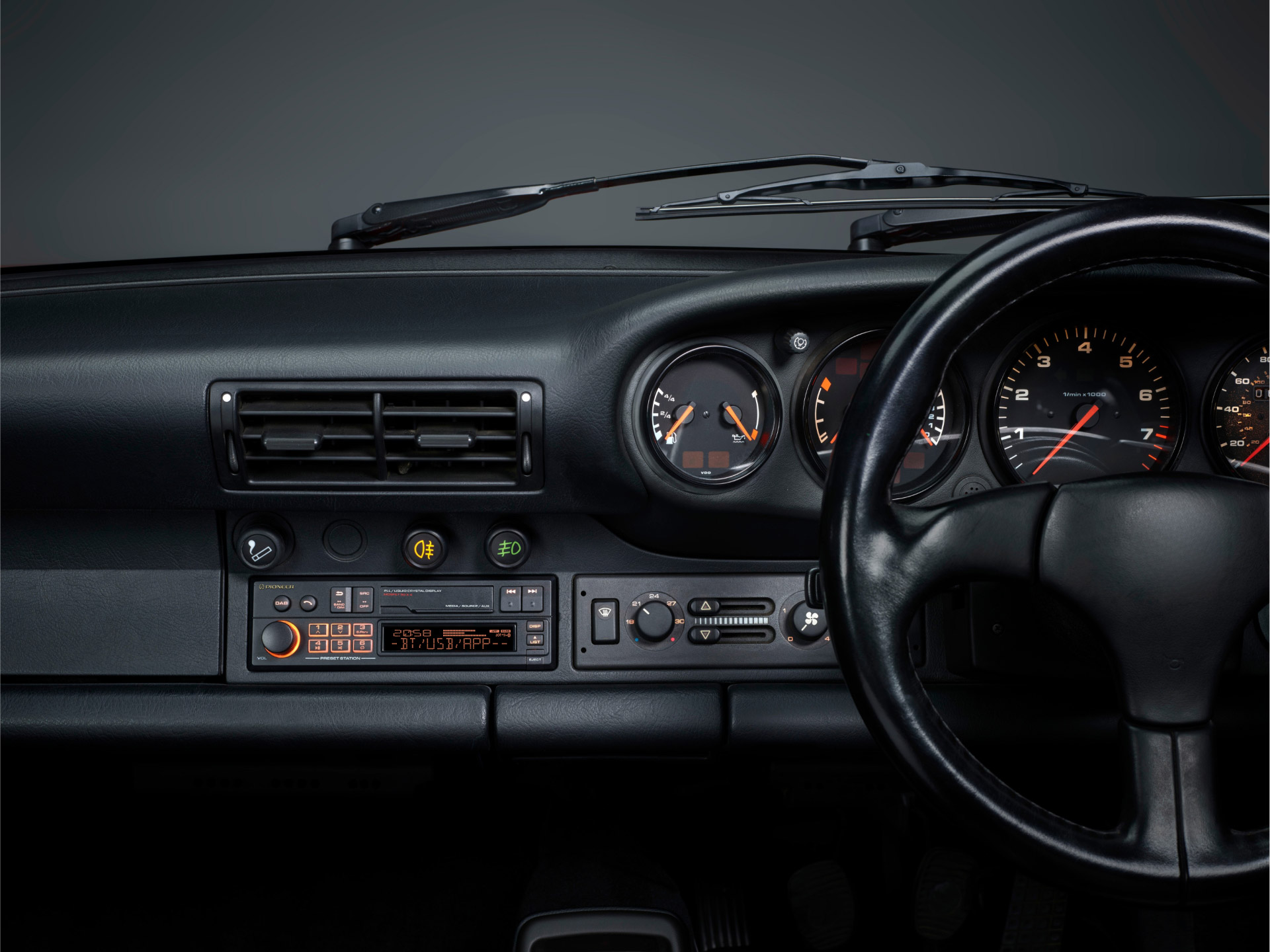 Autointerieur mit Armaturenbrett, Anzeigen, Lenkrad. Schwarzes Armaturenbrett, Radio und Lüftungsschlitze sichtbar. Scheibenwischer oben.