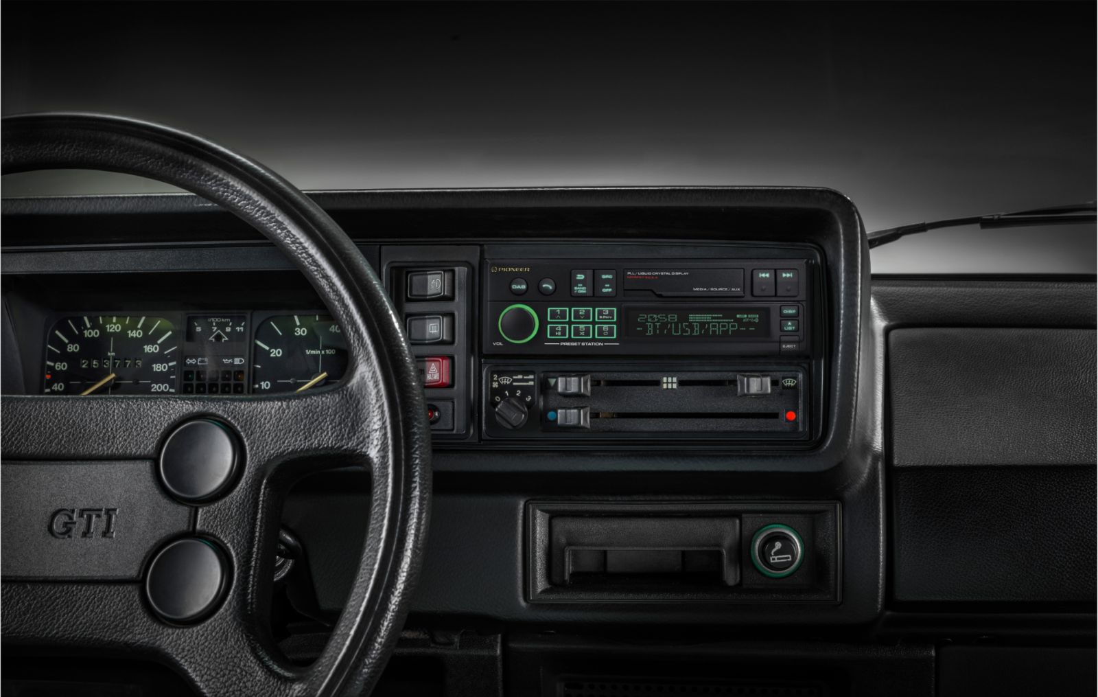 Auto-Innenraum. Schwarzes Lenkrad, Armaturenbrett mit Anzeigen und Radio. GTI-Logo links. Pioneer-Radio mit Display.