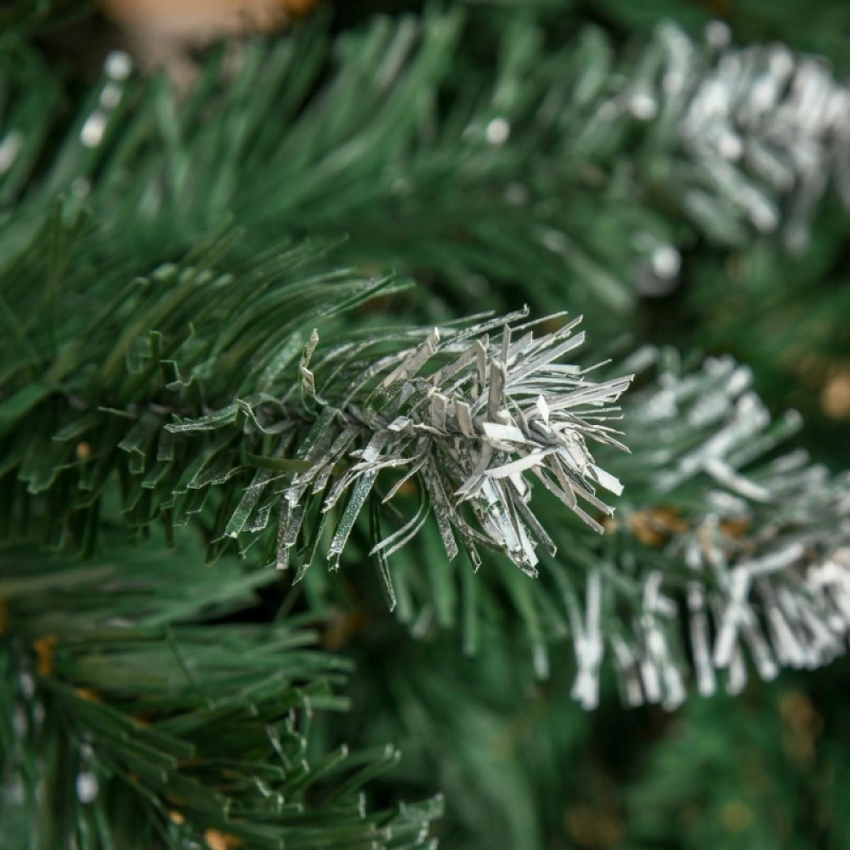 Nahaufnahme eines grünen Weihnachtsbaumzweigs mit weißen, vereisten Akzenten. Der Hintergrund ist verschwommenes grünes Laub.