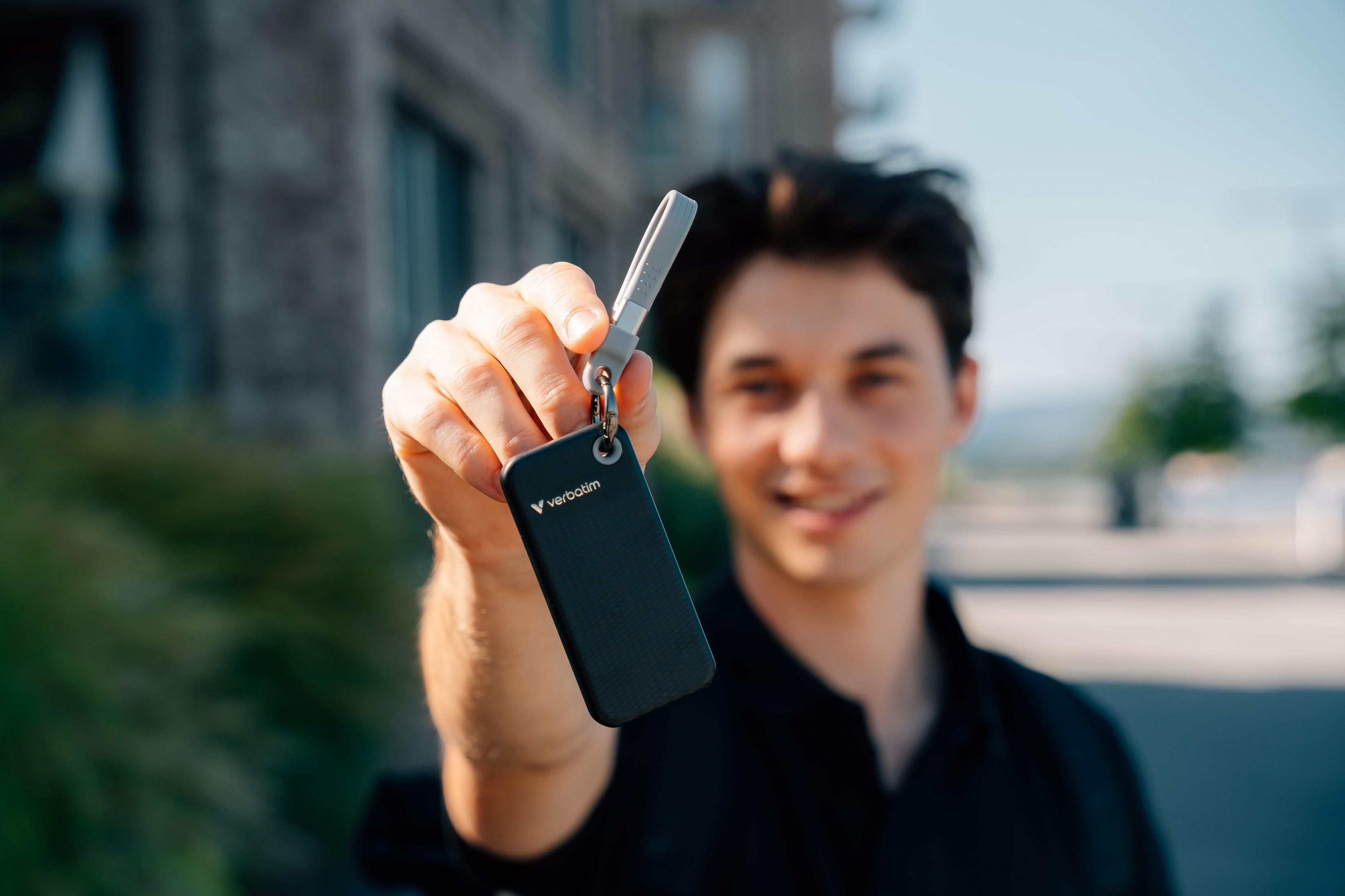 Mężczyzna trzyma klucz Verbatim. Uśmiecha się do kamery. Budynek i niebo w rozmytym tle.
