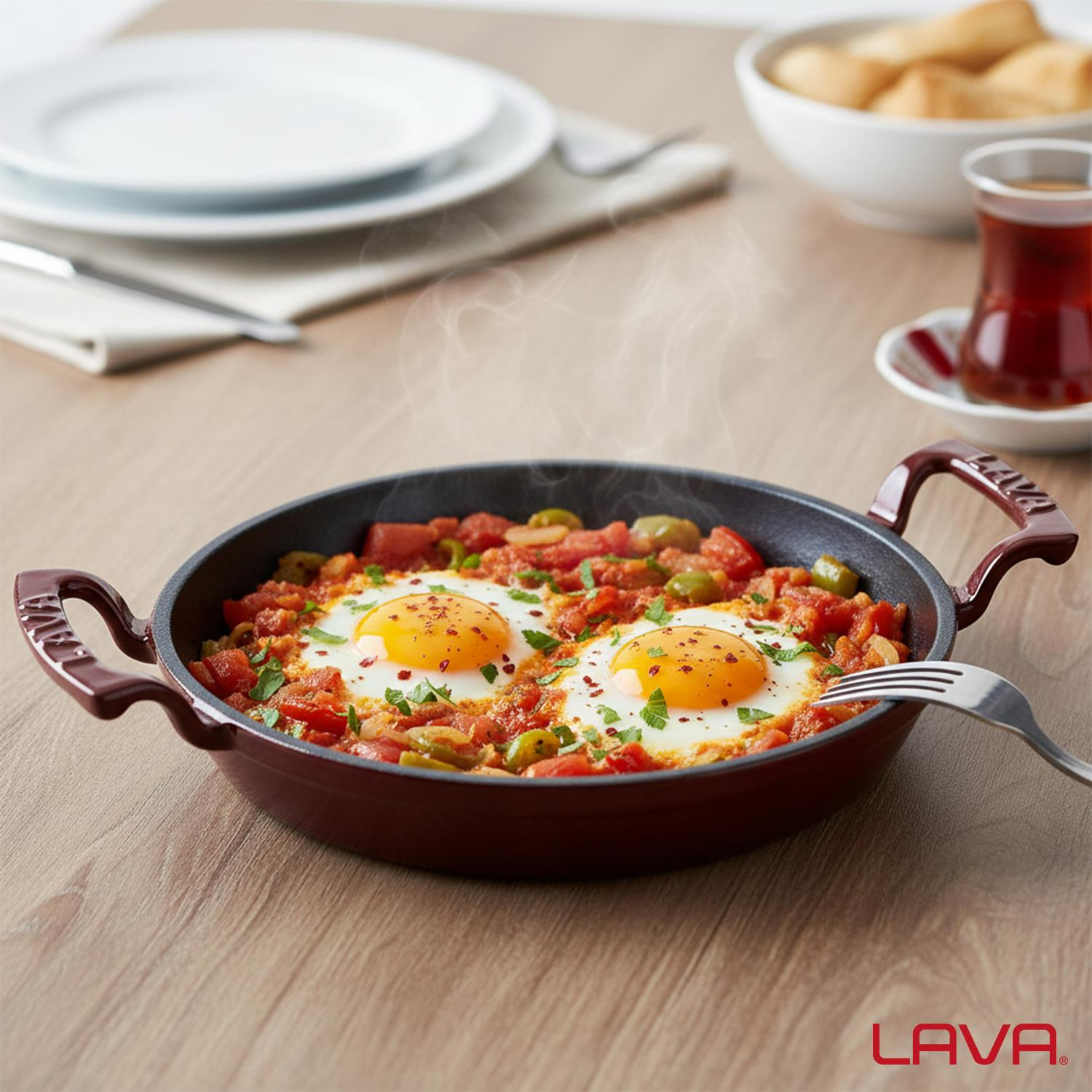 Kırmızı tavada domates soslu ve zeytinli iki kızarmış yumurta. Tabaklar, ekmek ve çay da ahşap masada.