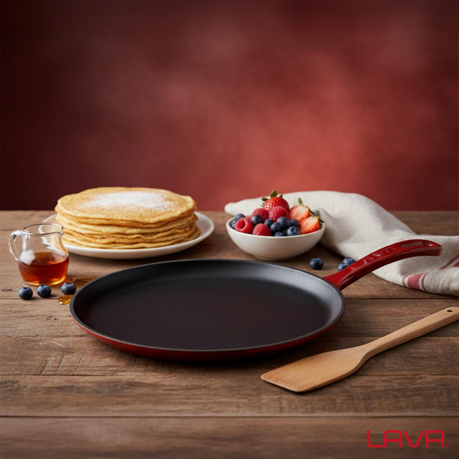 Ahşap bir masada krepler, meyveler, şurup ve bir tava. Bir kasede meyveler ve bir kavanozda şurup. Kırmızı saplı tava ve spatula.