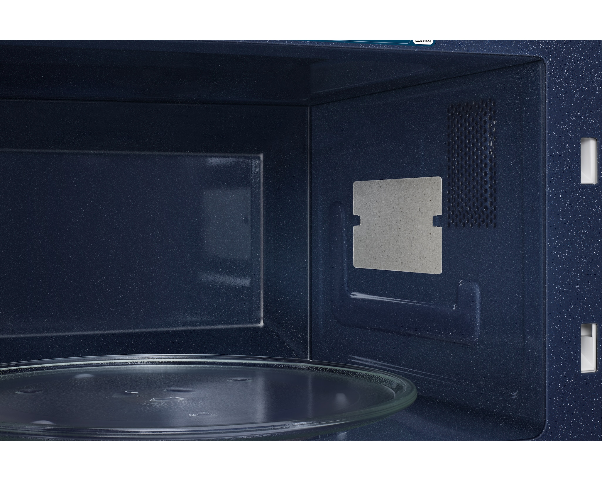 Interno di un forno a microonde blu navy. Un piatto di vetro sul fondo. Ventilazione e luce rettangolare visibili.