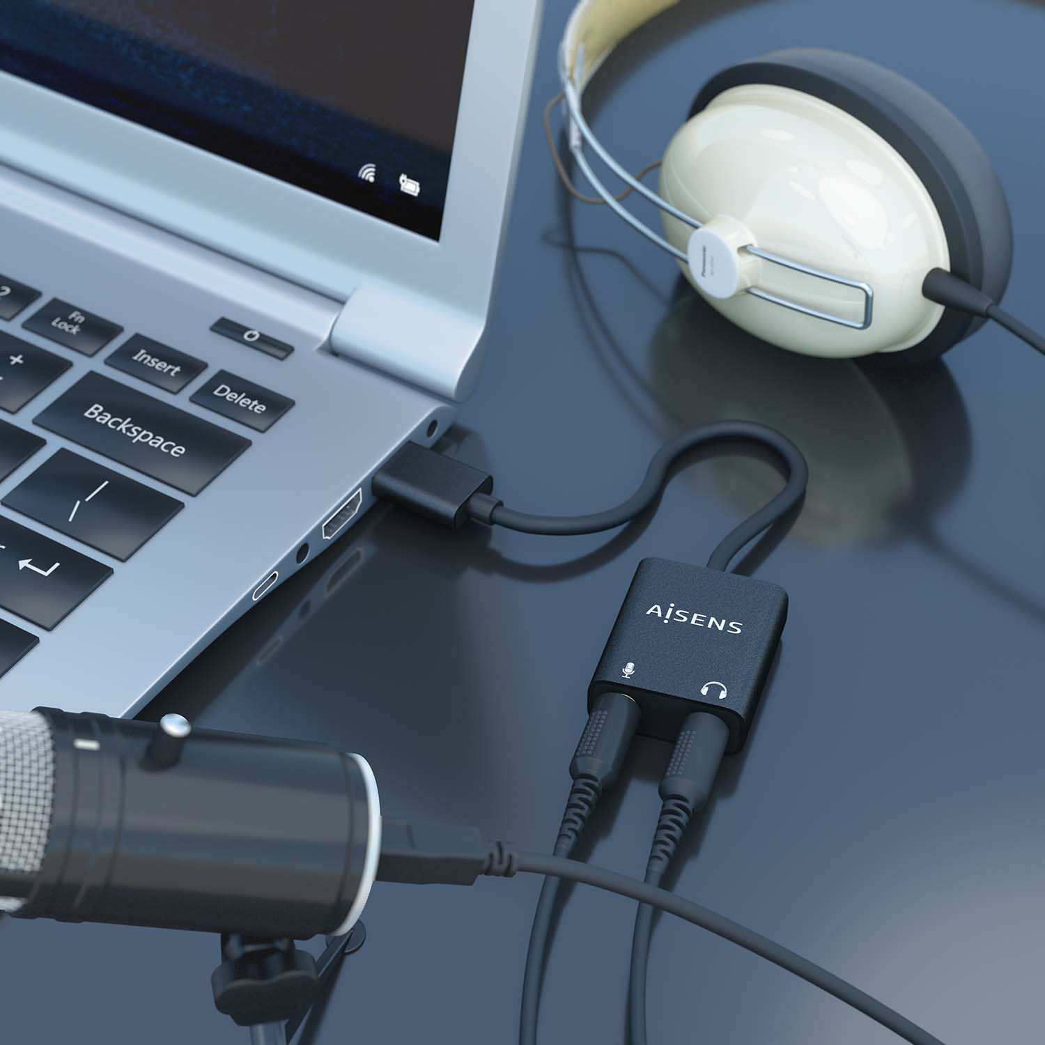 Portátil con auriculares, micrófono y adaptador de audio. Tonos negros y plateados dominan sobre una superficie oscura reflectante.