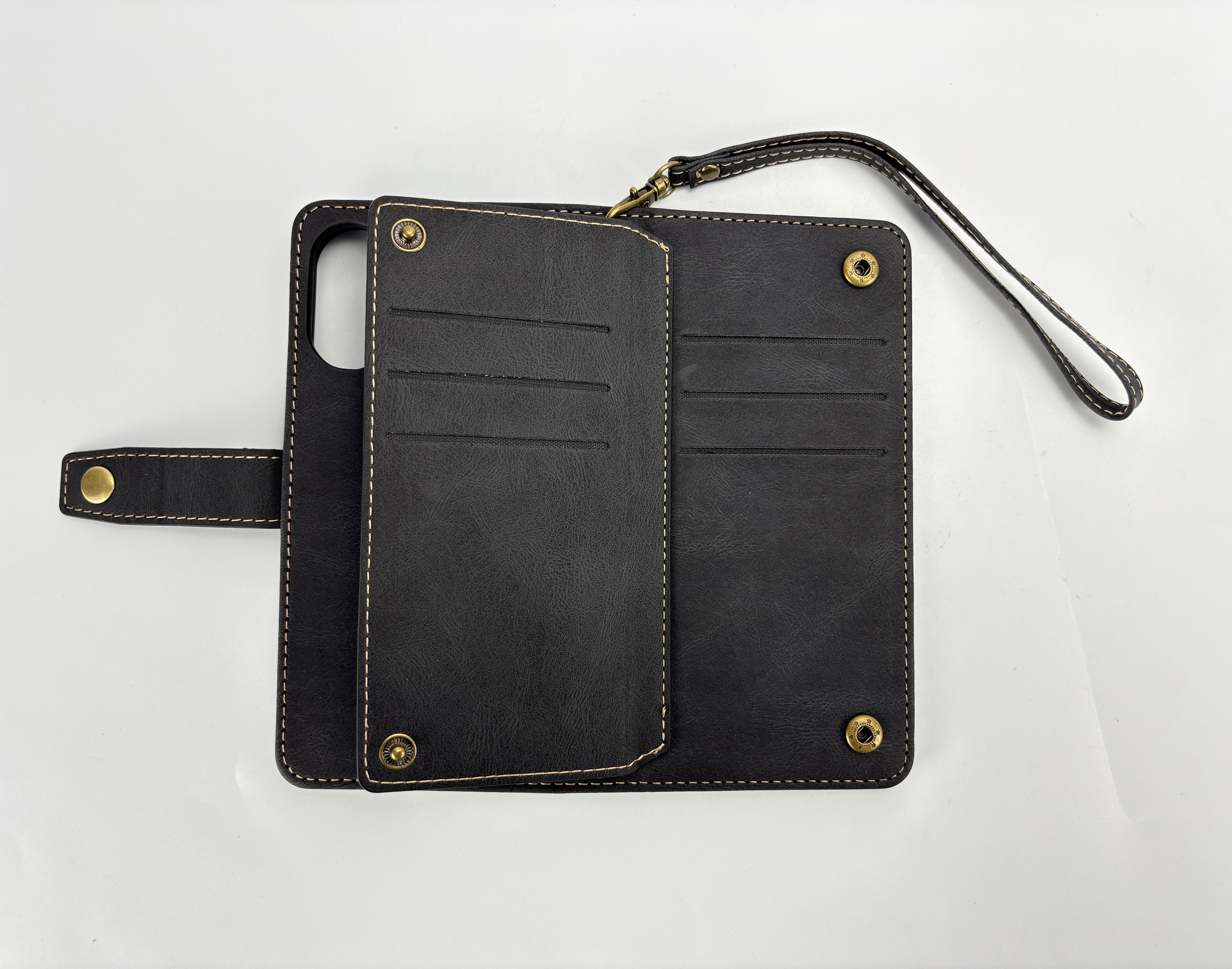 Custodia per telefono in pelle nera con cinturino, aperta su sfondo bianco. Cuciture visibili e hardware in ottone.