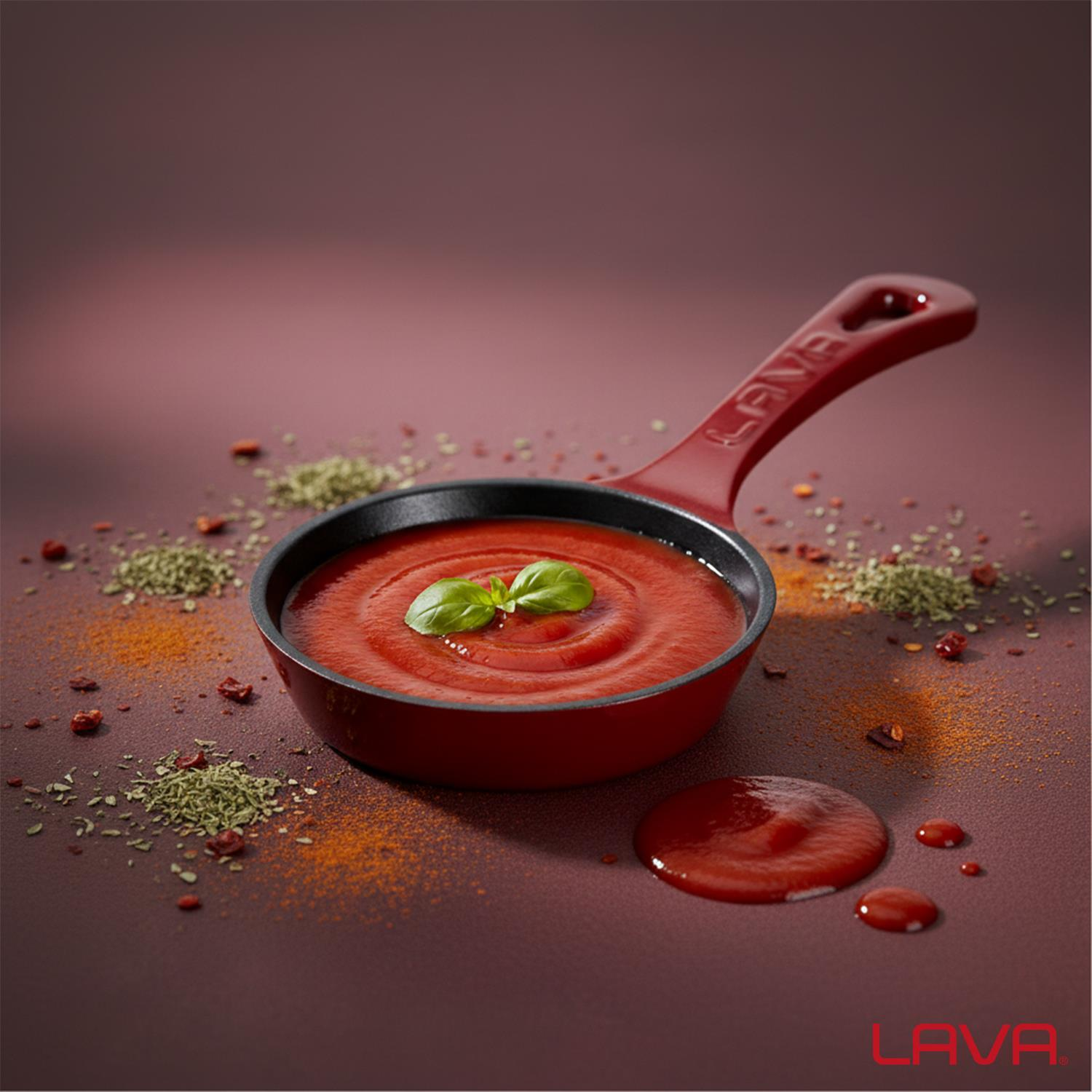 Domates sosu ve fesleğenli küçük kırmızı tava. Baharatlar etrafa dağılmış. Tavanın bir sapı var ve altta 'LAVA' yazıyor.